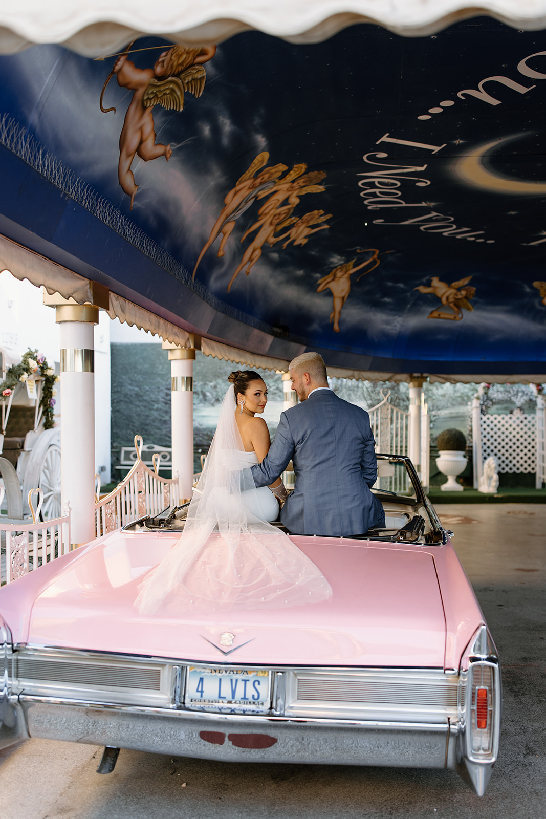 Bride and groom sit on the back of a pink convertible