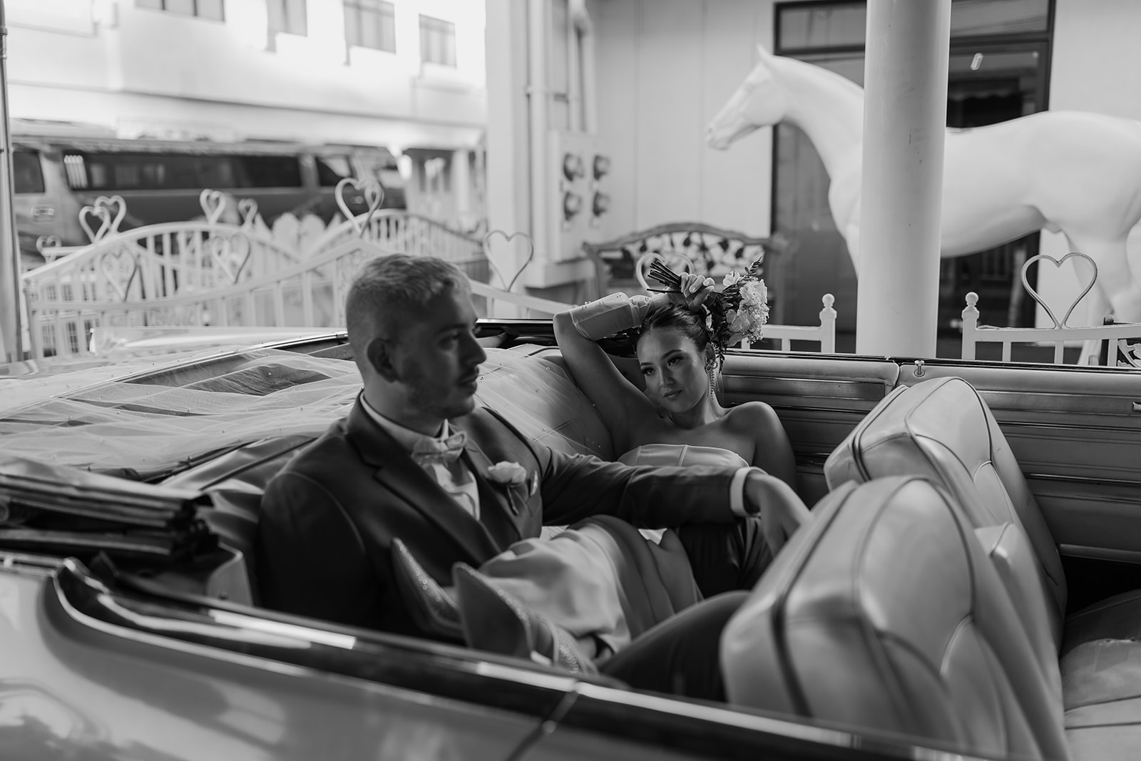 Bride and groom sit in the back of a convertible