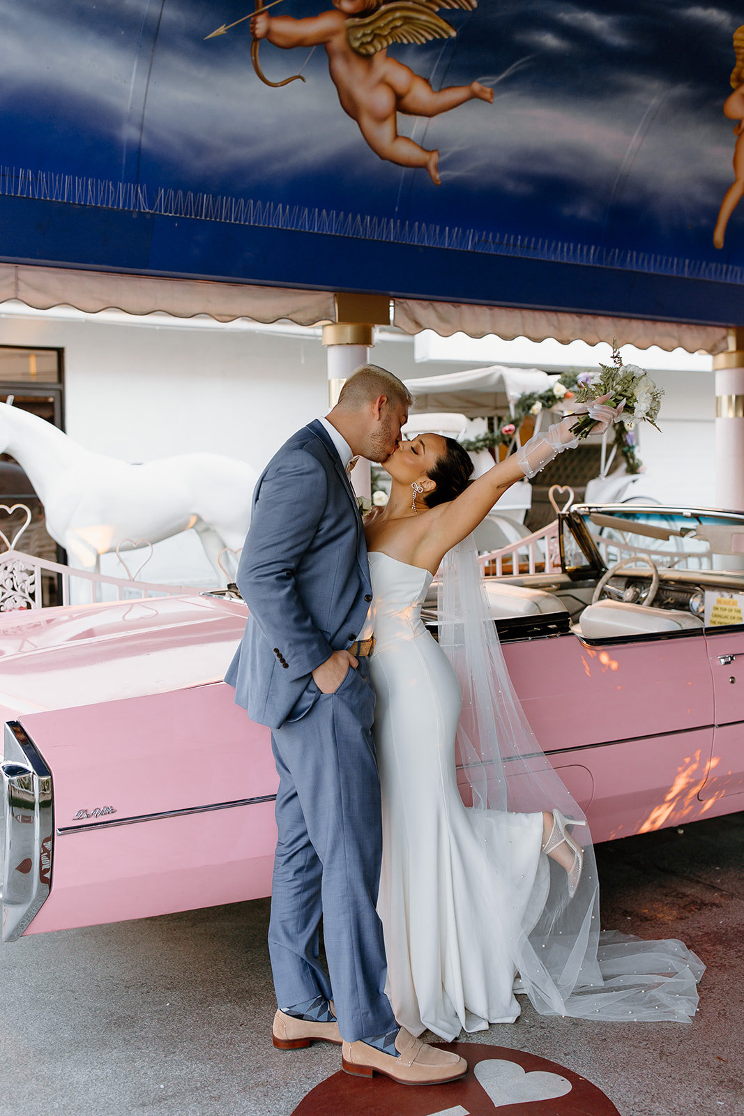 Bride and groom kissing in front of a pink convertible