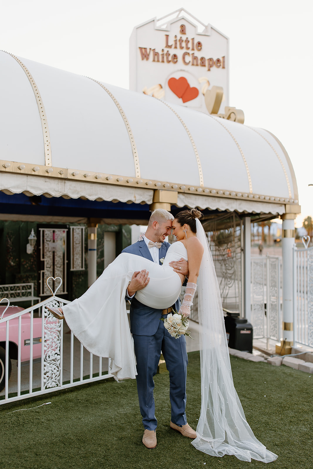 Groom holds his bride in front of the little white chapel sign