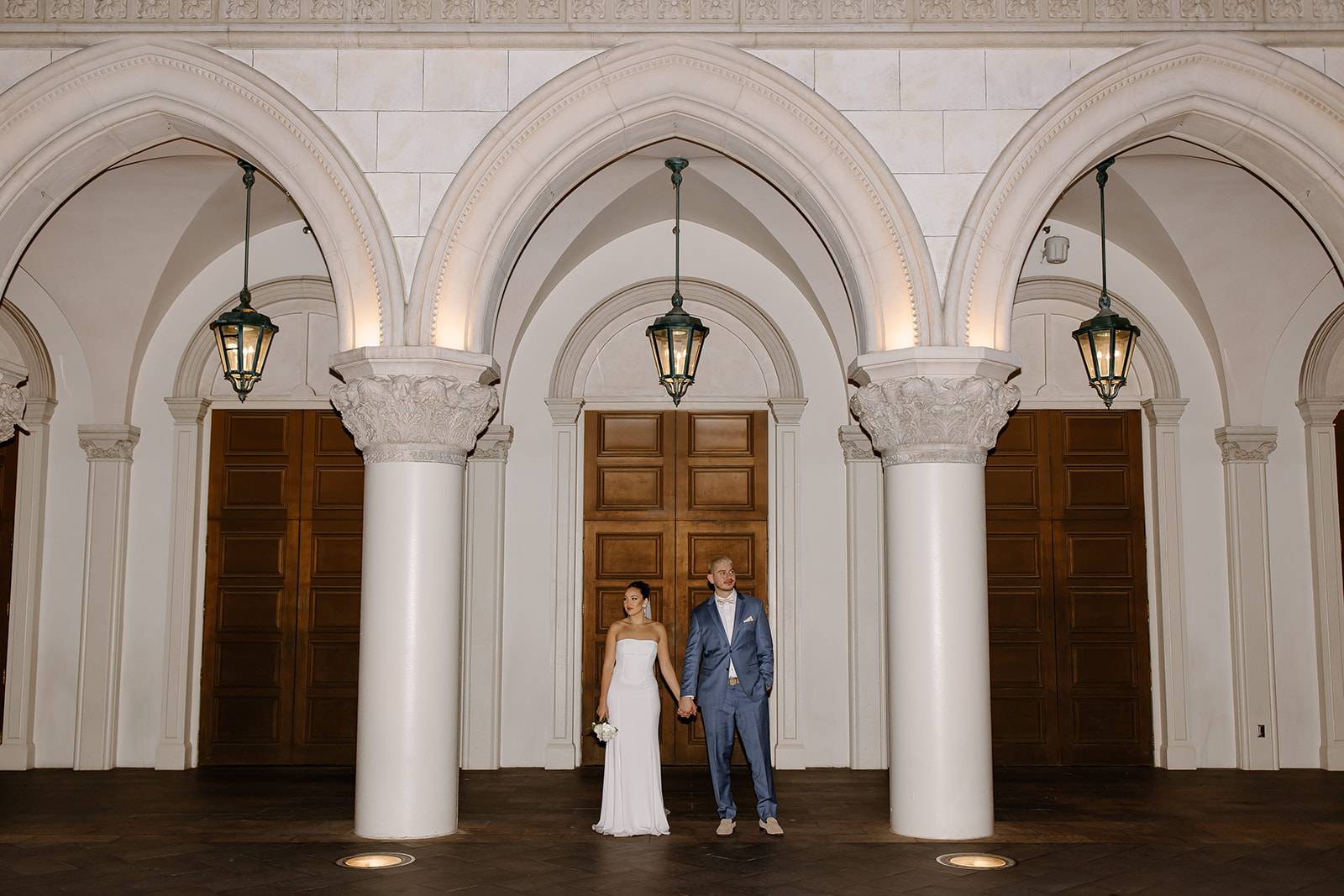 Bride and groom holding hands underneath pillar arches