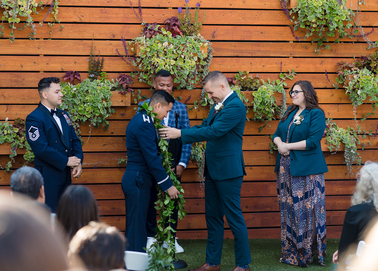 An outdoor ceremony at the Vue, one groom places a wreath of leaves over his husbands neck as a nod to his culture.