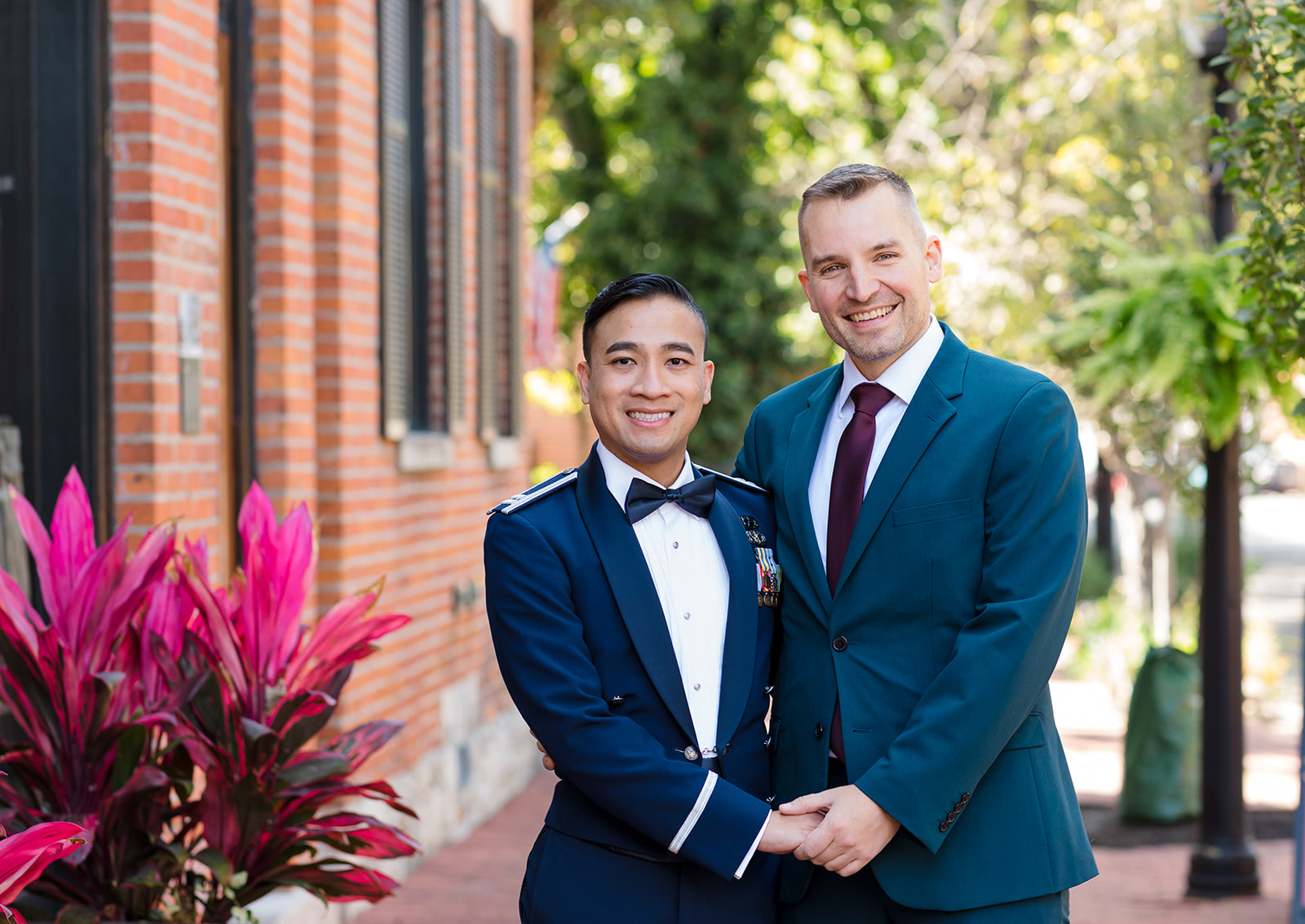 Two grooms hold hands and smile at the camera