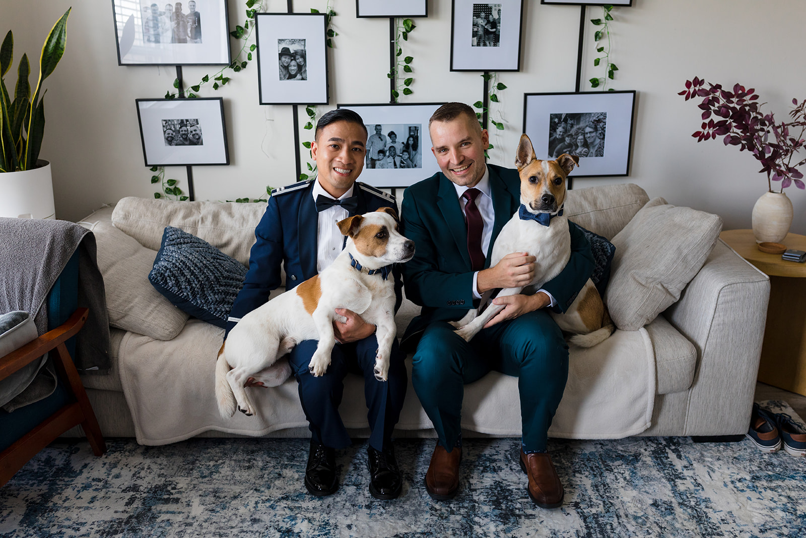 Two grooms pose at home on their couch with their two dogs on their wedding day. 