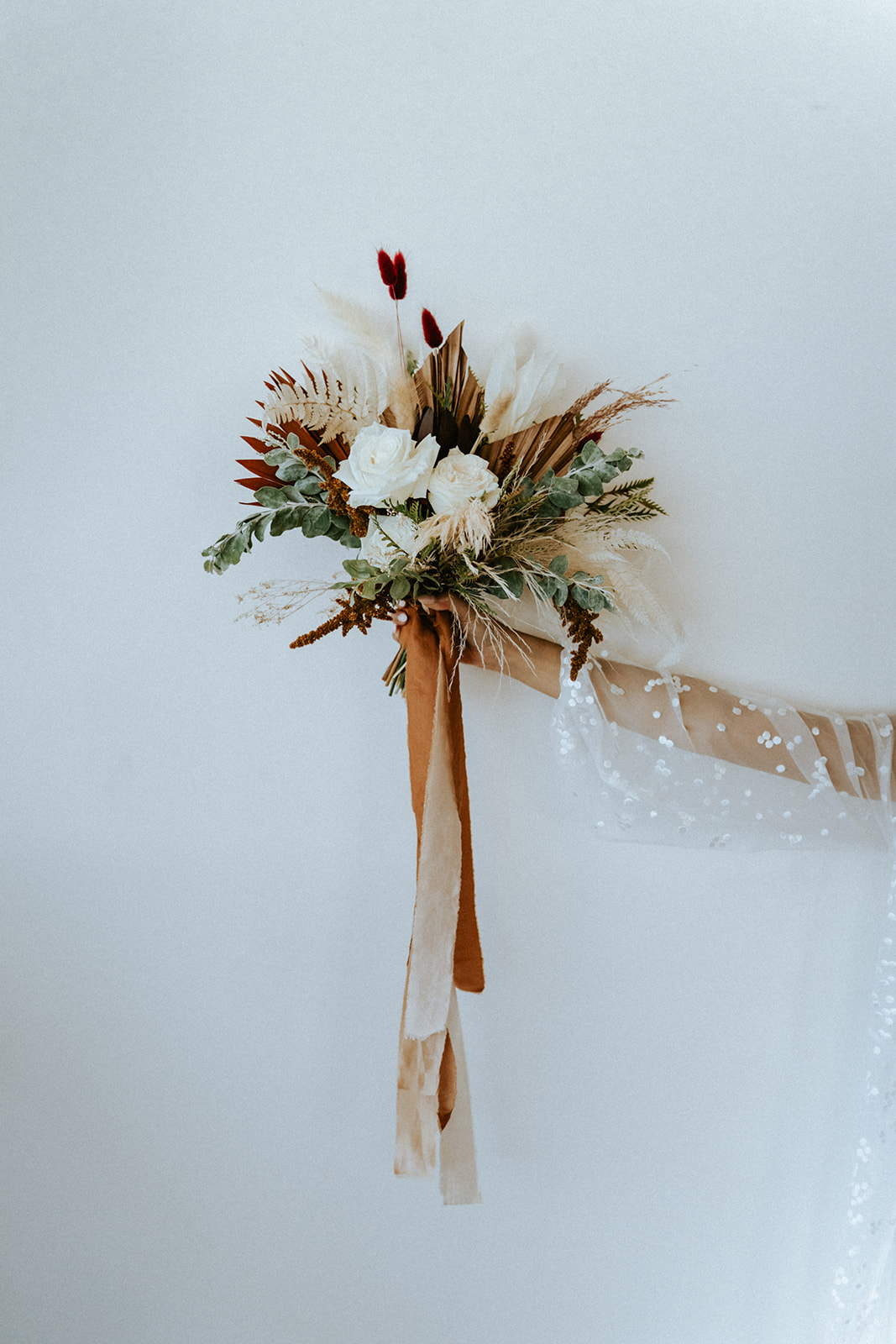 Bride holding a Boho bouquet with pops of rustic orange against a clean background