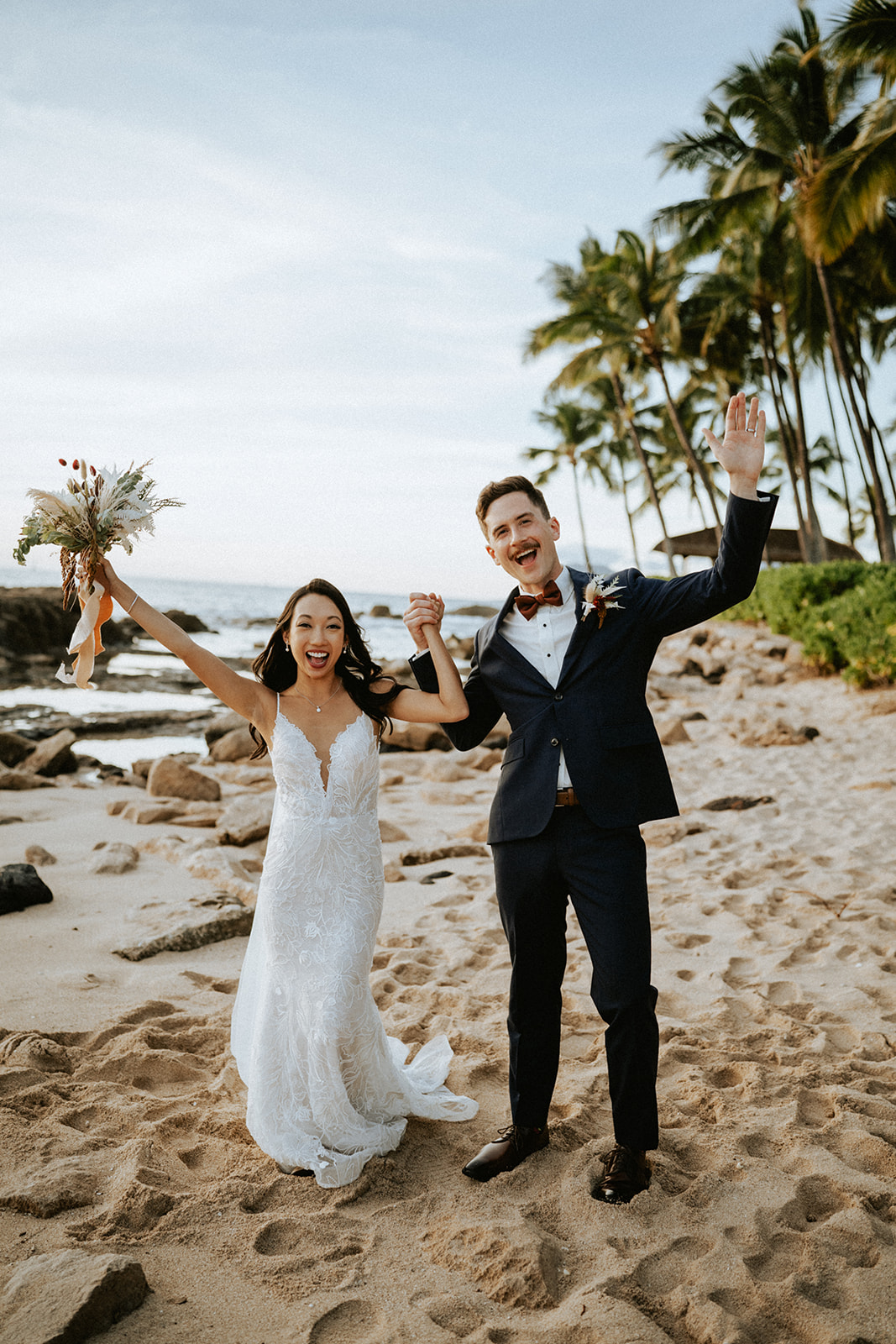 Bride and groom celebrating on the beach fronting Lanikuhonua during sunset