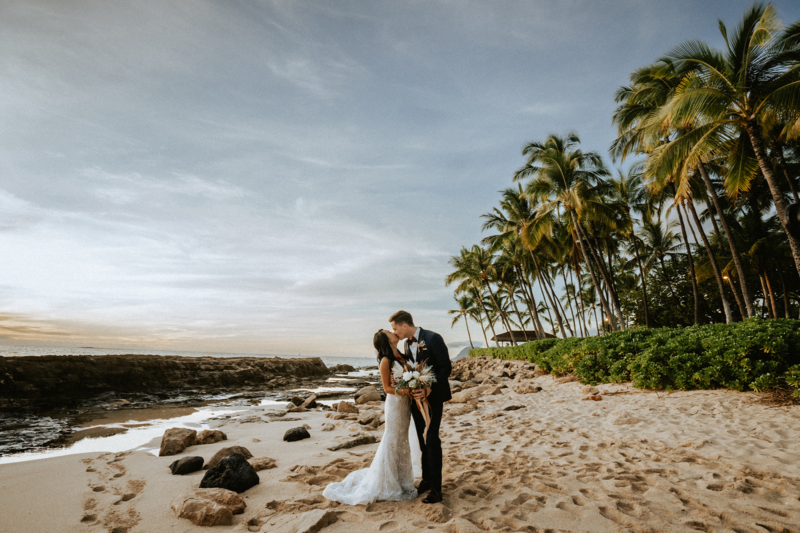 Bride and groom stroll out on the beach fronting Lanikuhonua during sunset