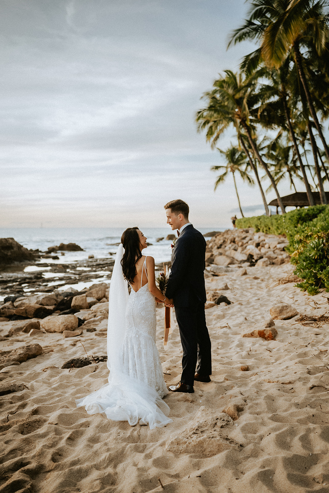 Bride and groom stroll out on the beach fronting Lanikuhonua during sunset