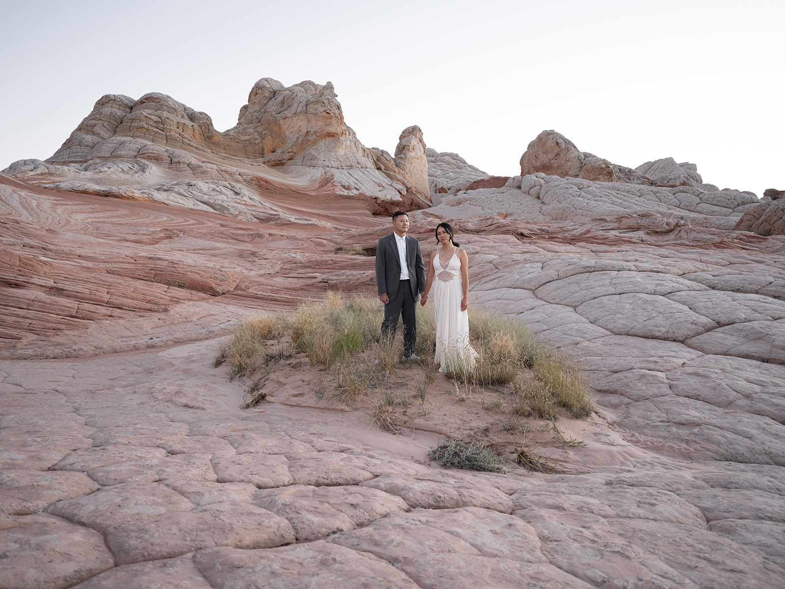Couple standing in a small patch of grass surrounded by a sea of petrified sand dunes in White Pocket Arizona 
