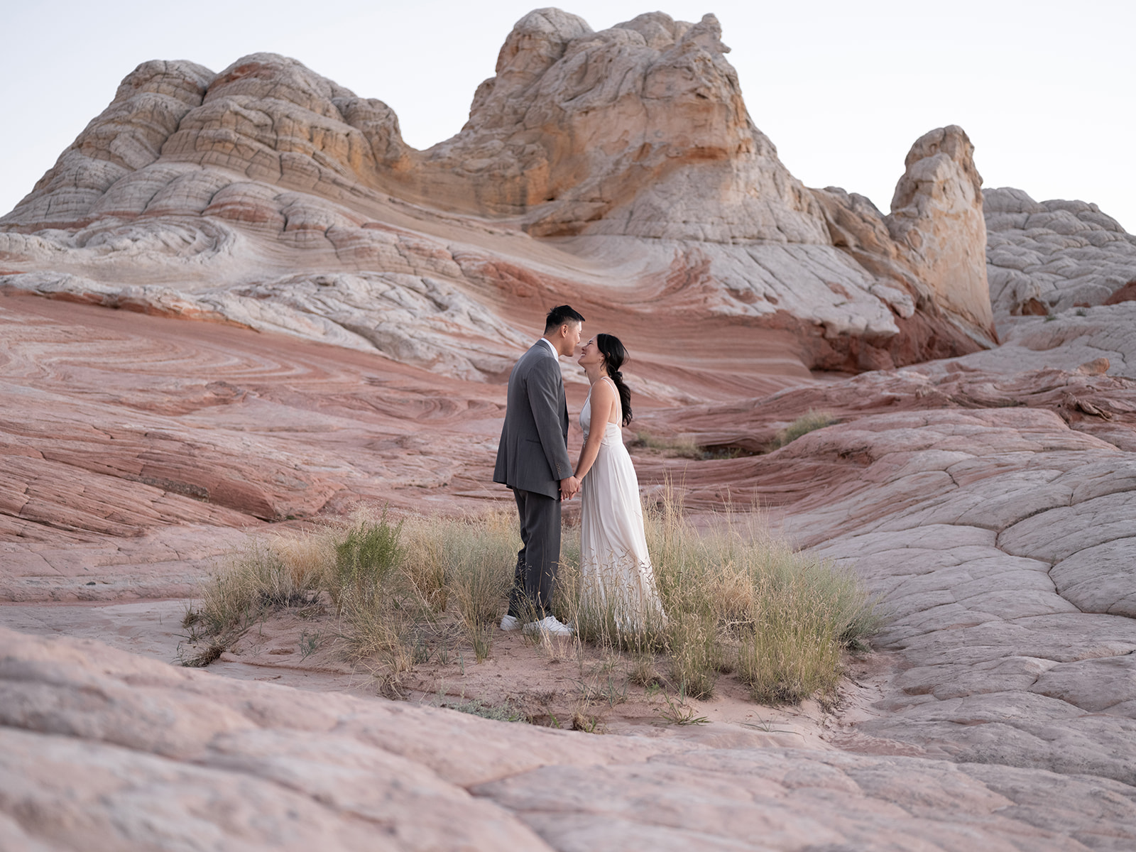 Couple kissing in a small patch of grass surrounded by a sea of petrified sand dunes in White Pocket Arizona 