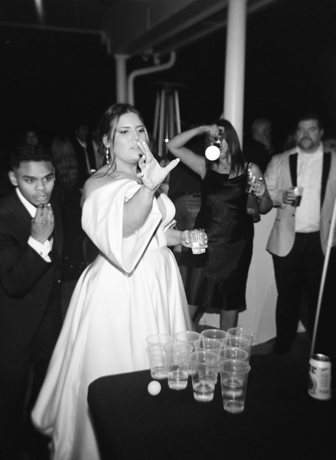a black and white flash film photo of the bride playing beer pong with her wedding guests. a candid moment.