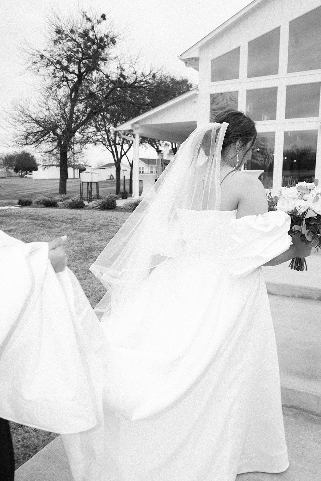 black and white photo of the bride and her long dress and train walking up to the glass wedding venue