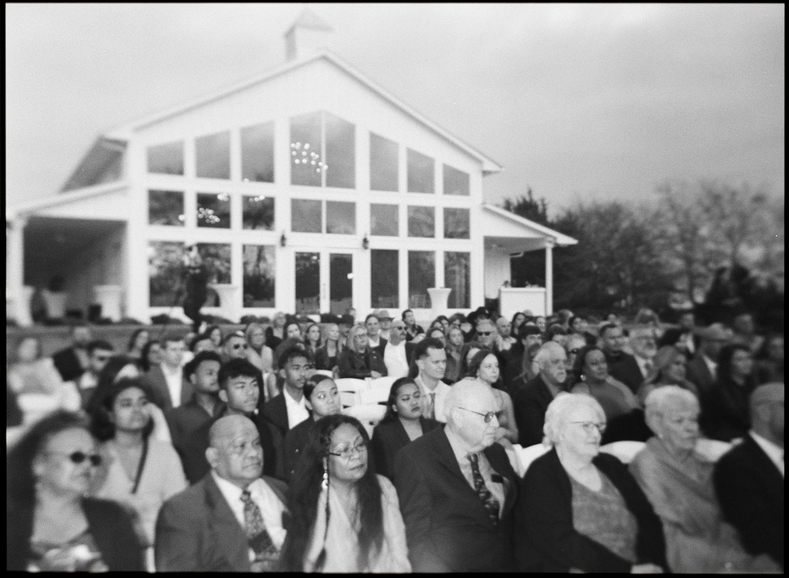 a medium format Holga film photo of the guests with the glass wedding venue in the background