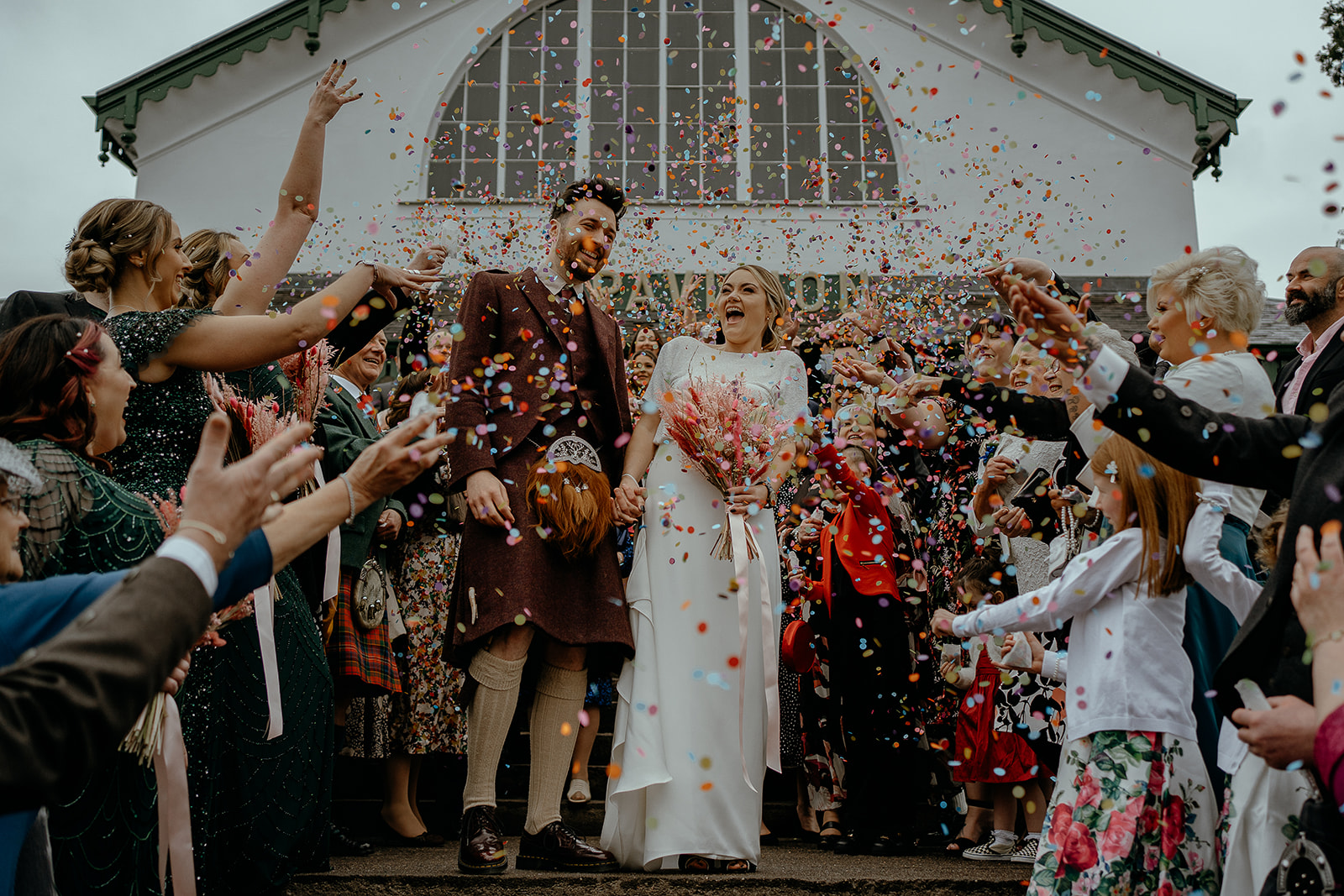 bride and groom get covered in bright colourful confetti thrown by wedding guests