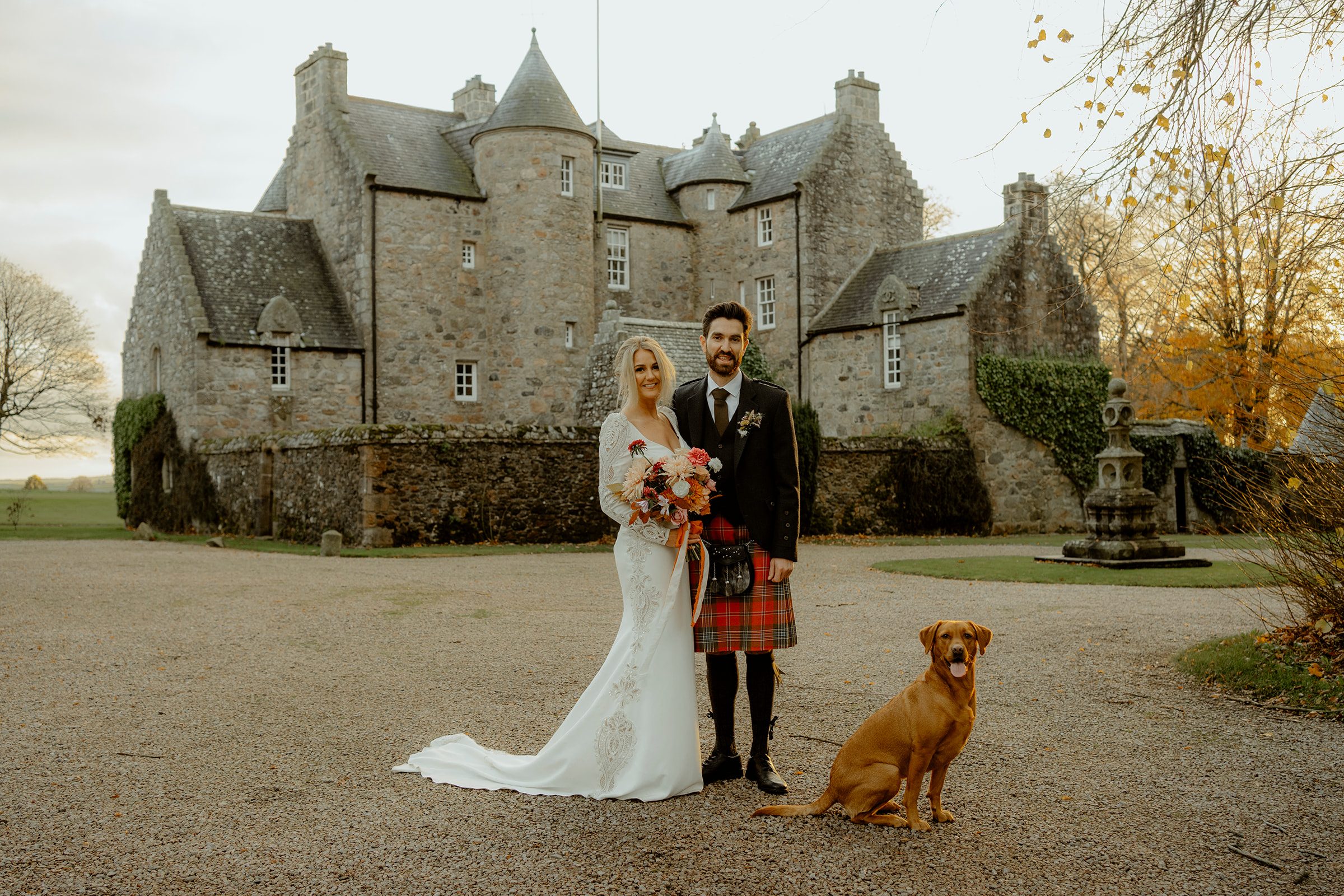 Bride and Groom holding each other next to dog infront of castle