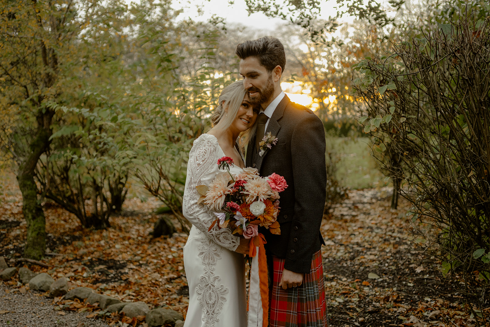 Bride and Groom hold each other underneath trees in Autumnal light