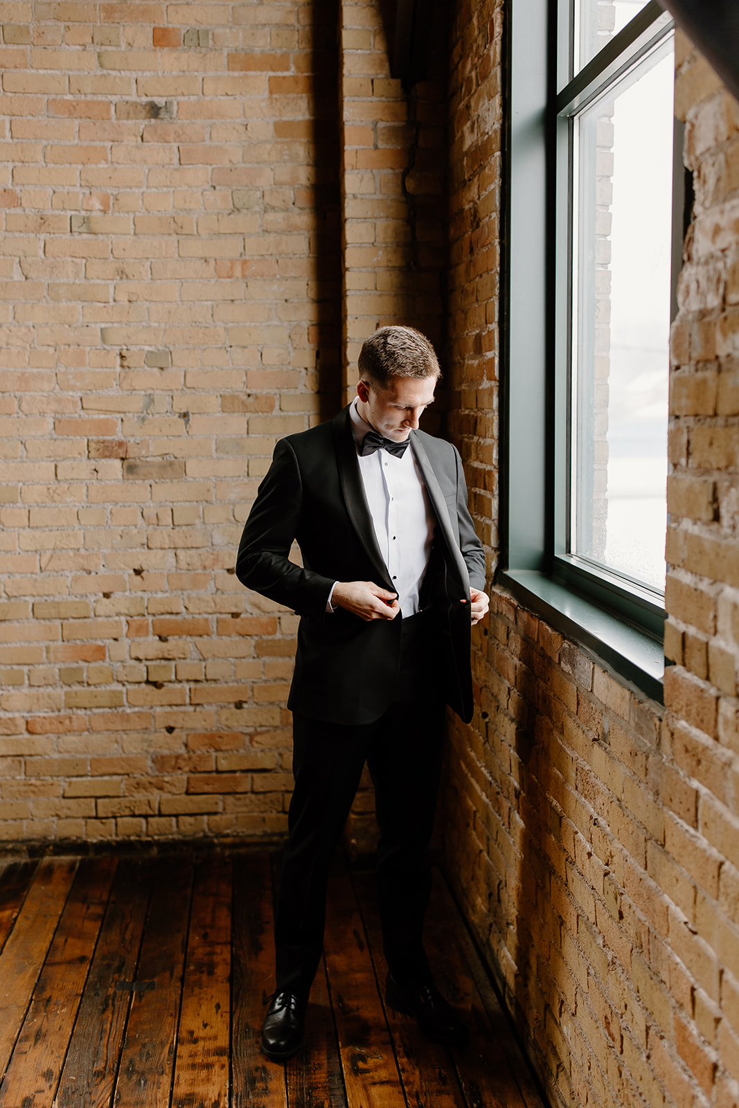 Groom buttoning his jacket in front of a window