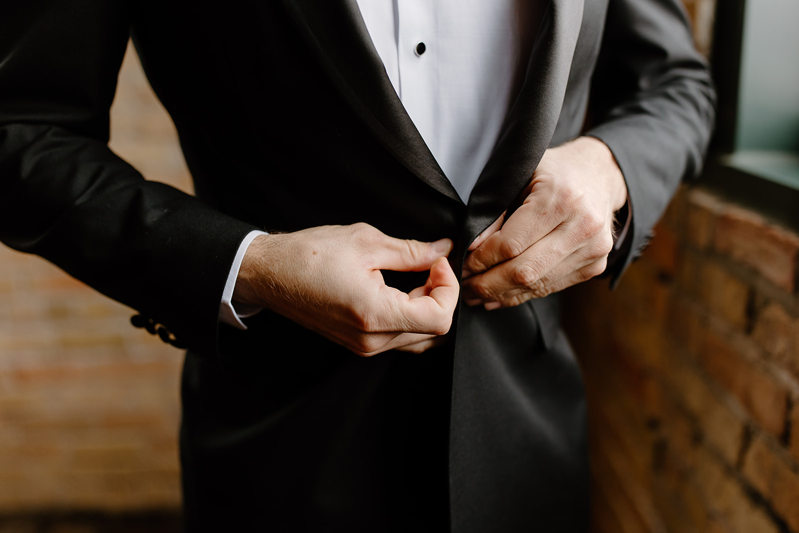 Groom buttoning his jacket in front of a window