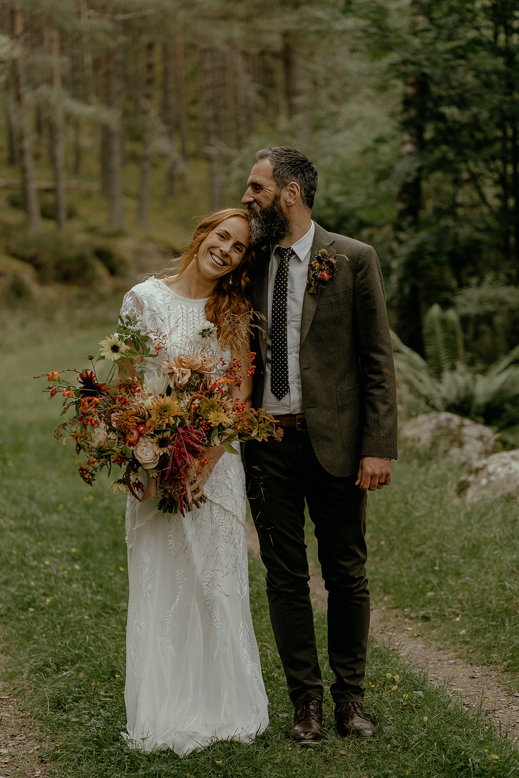 bearded groom kisses bride on the top of her head while she holds a beautiful bouquet of flowers