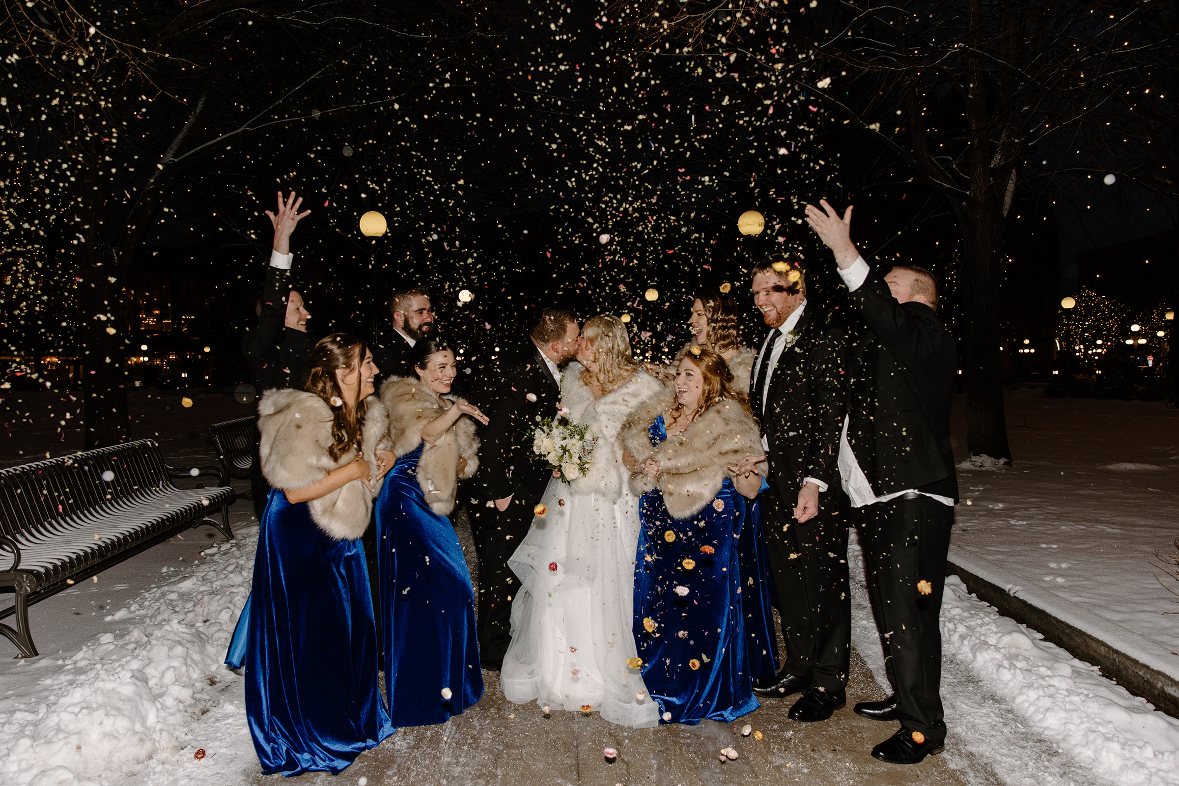 Wedding party cheer while bride and groom kiss during snow storm