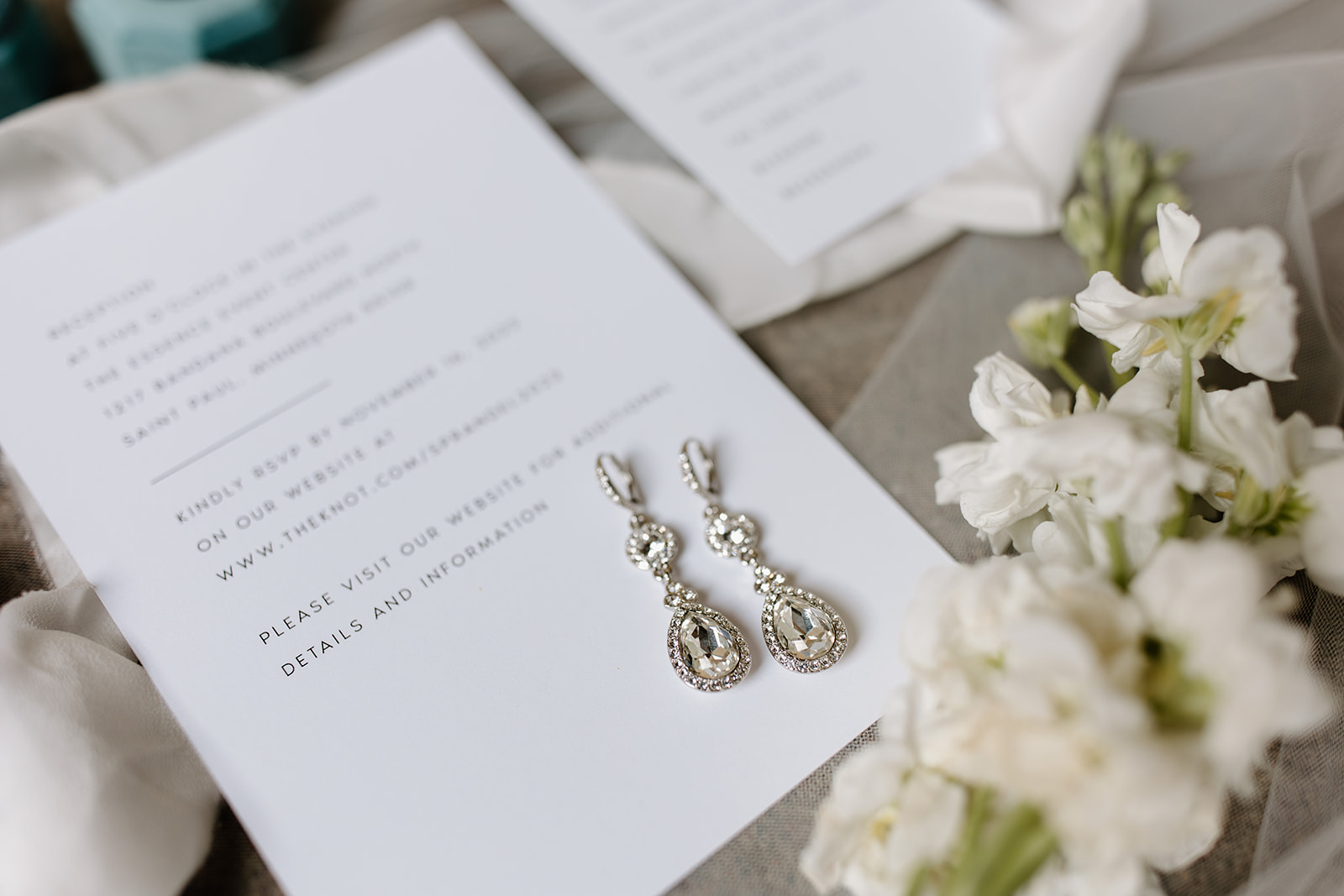 Flat lay of wedding invitations, jewelry, and shoes.