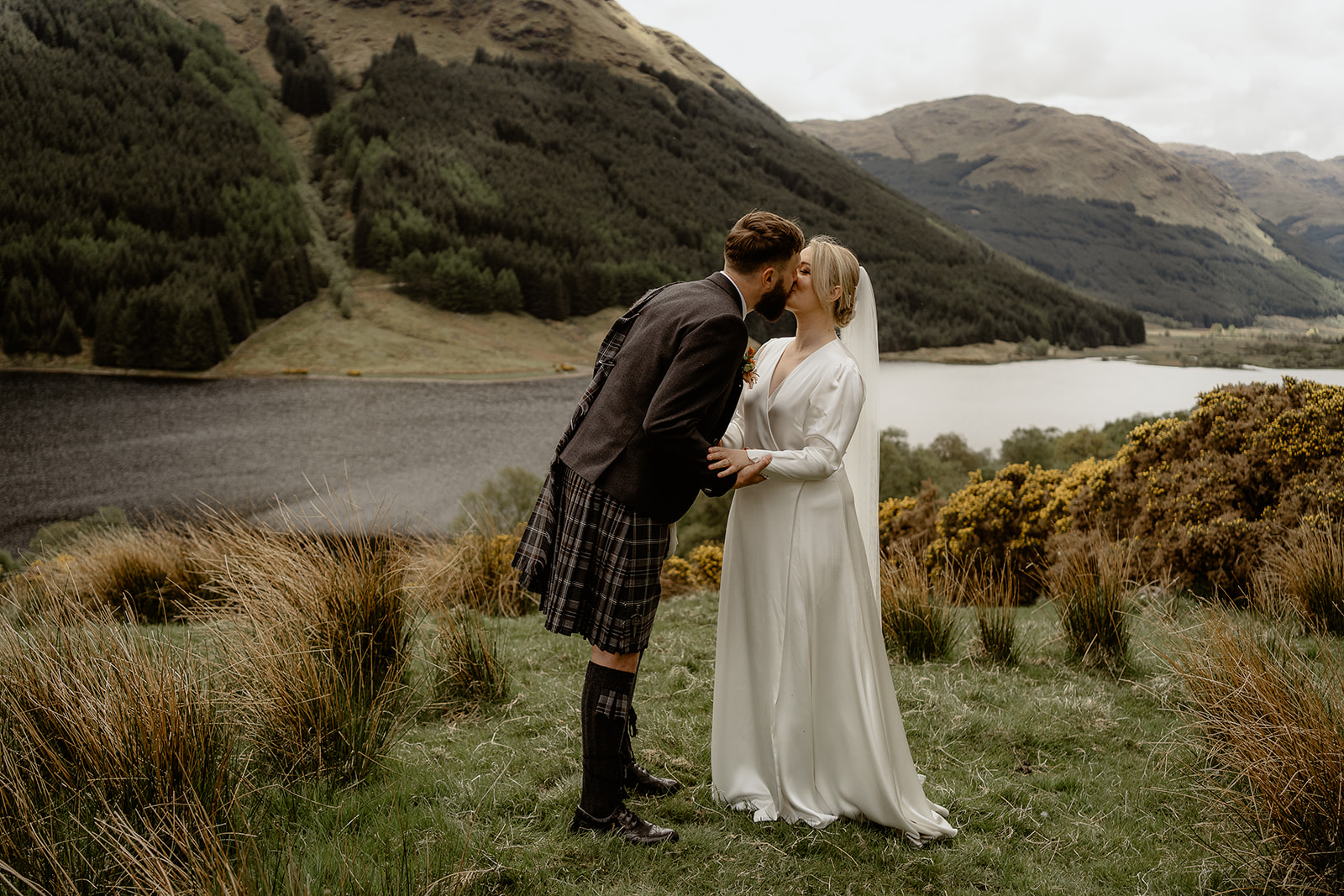 bride and groom share first kiss after tying the knot at monachyle mhor with loch and mountains in the background