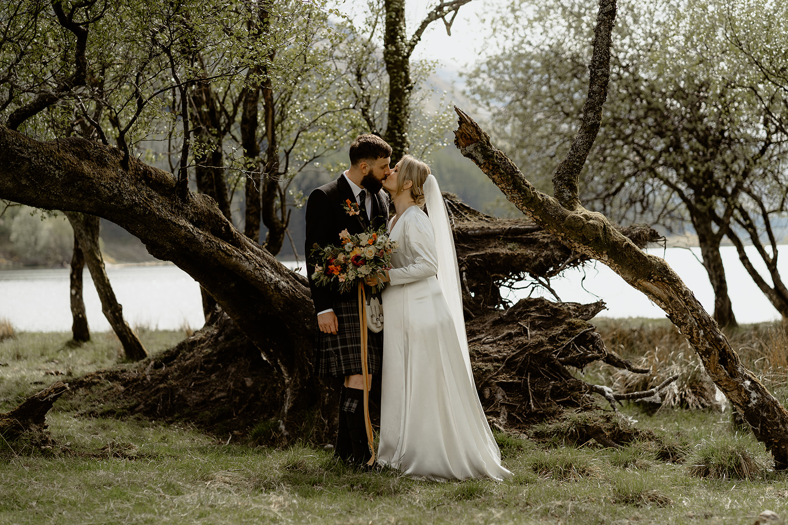 bride and groom kiss next to old fallen tree