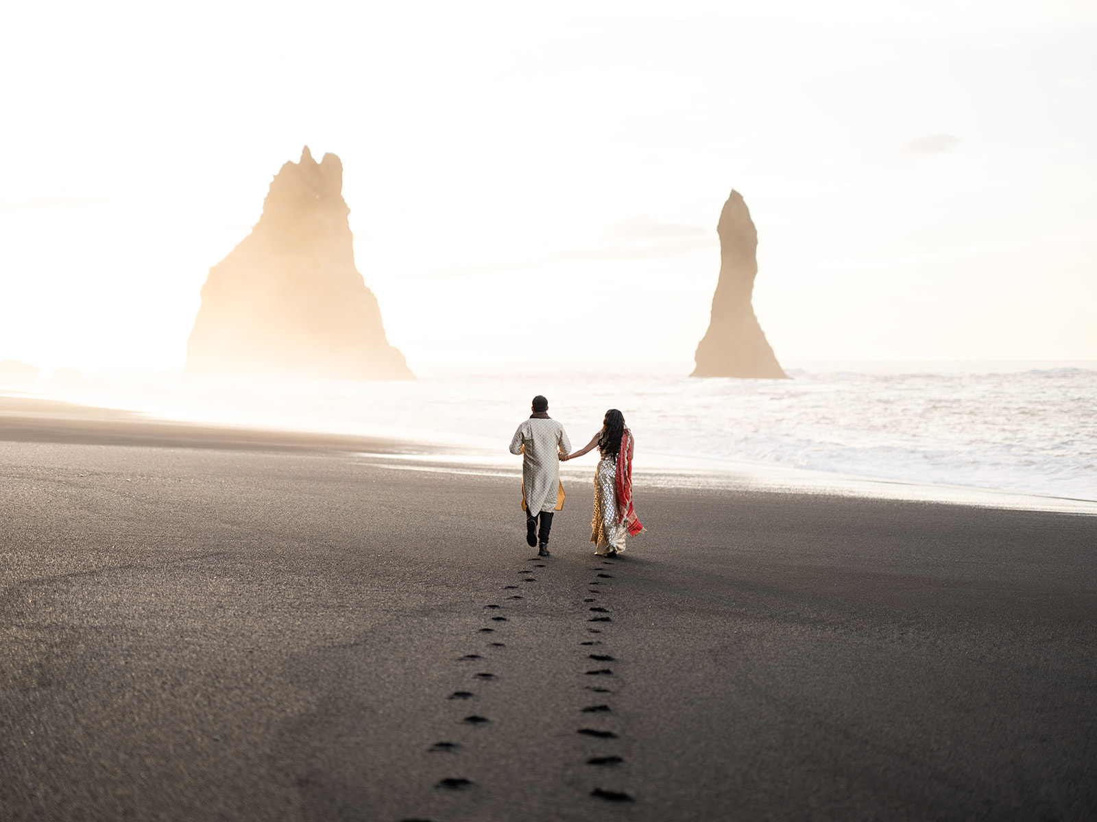 Bride and Groom walking on black sand beach during sunrise