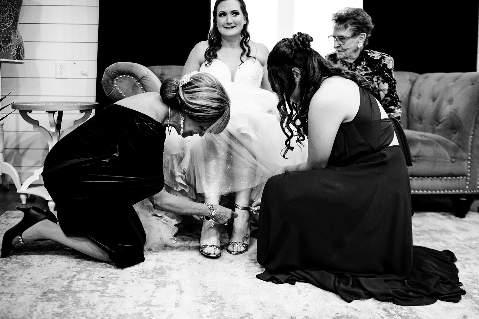 Brides, mother and bridesmaids, helping her put on her shoes