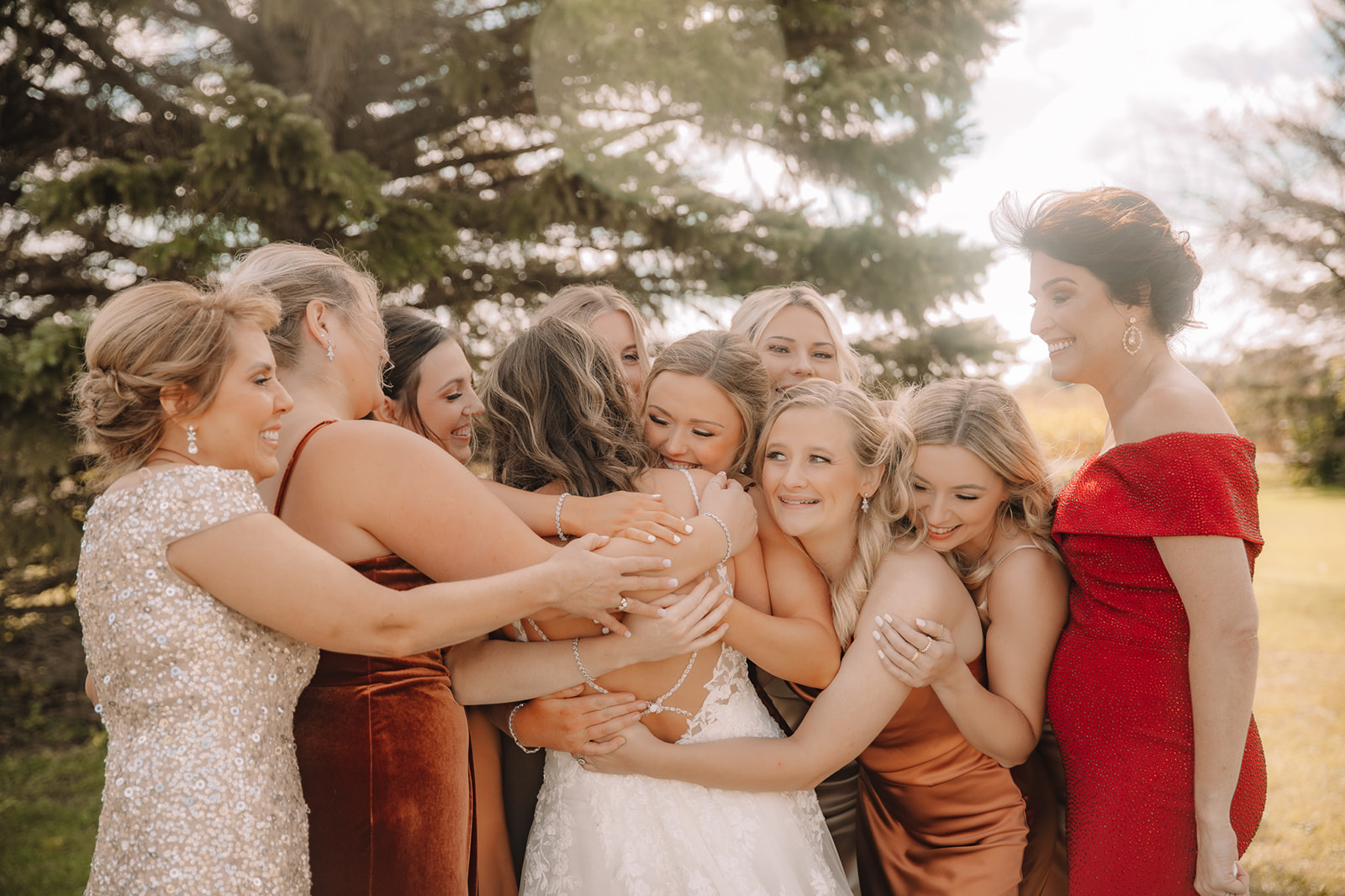 Bride surrounded by emotional hugs from bridesmaids after dress reveal.