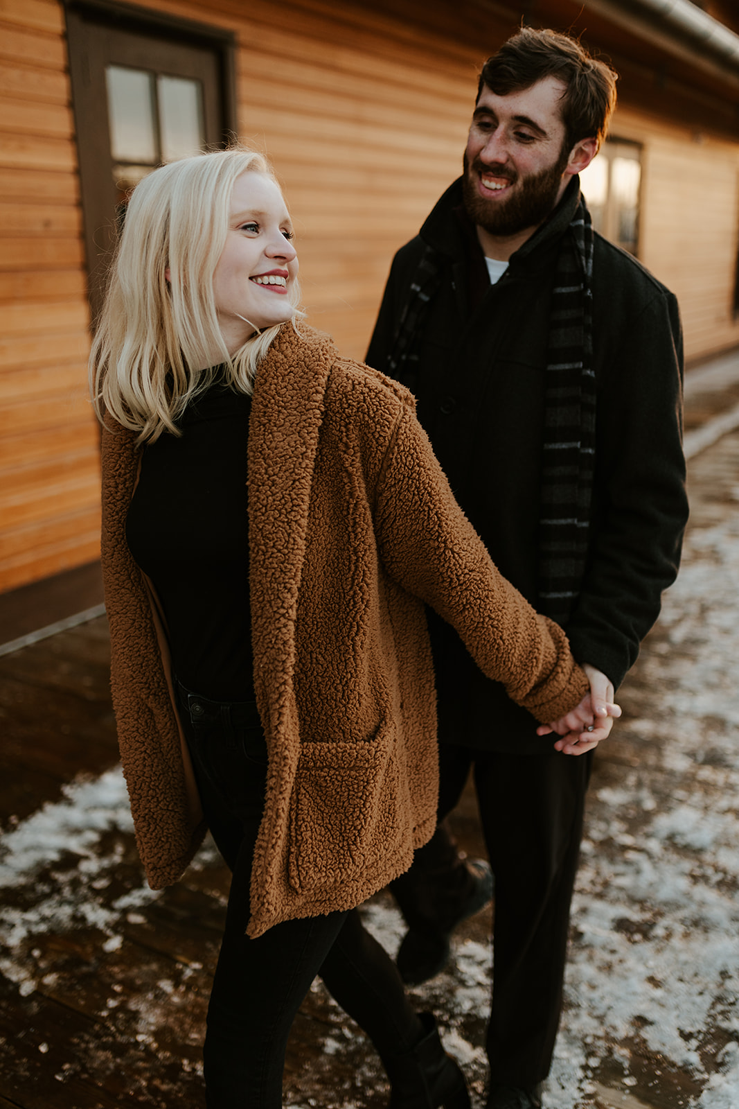 A couple doing engagement photos in Buffalo, NY walks along the harbor in the wintertime.