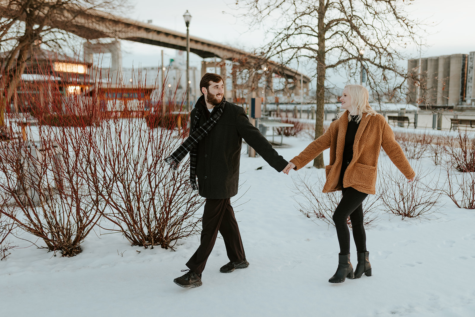 A couple doing their engagement photos in Buffalo, NY walks along a snowy path at Canalside.