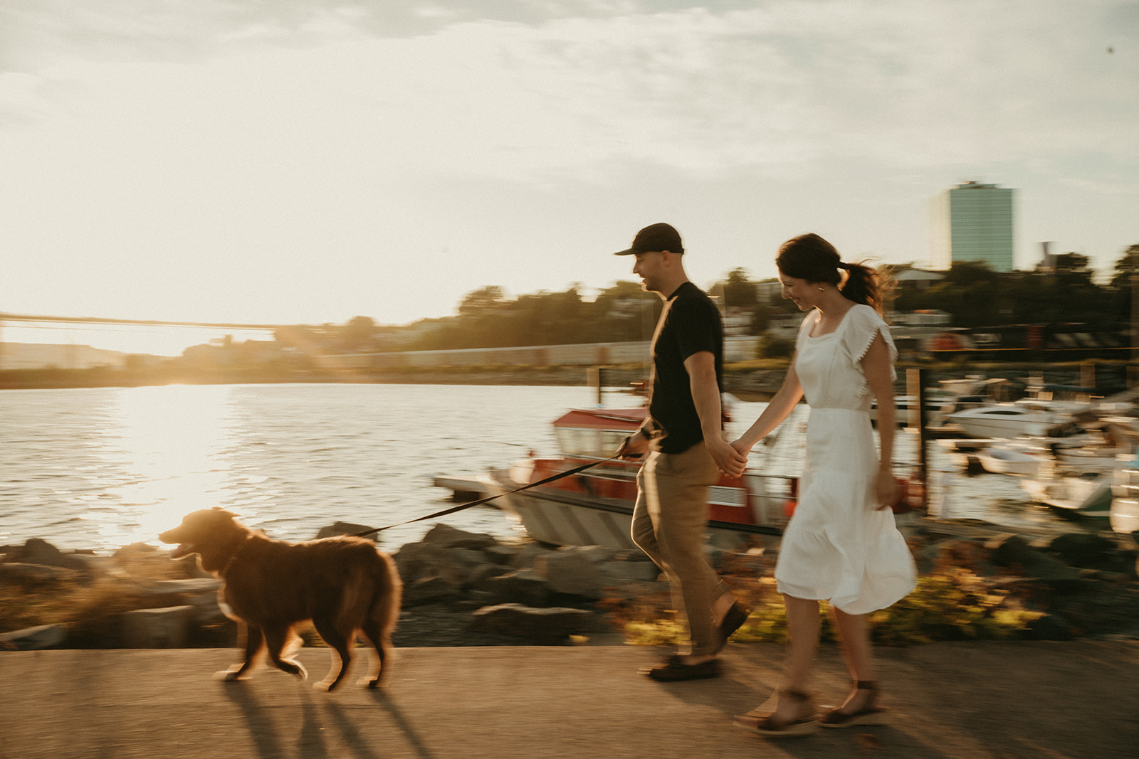 motion blur photo of couple running my the ocean and boats with their dog