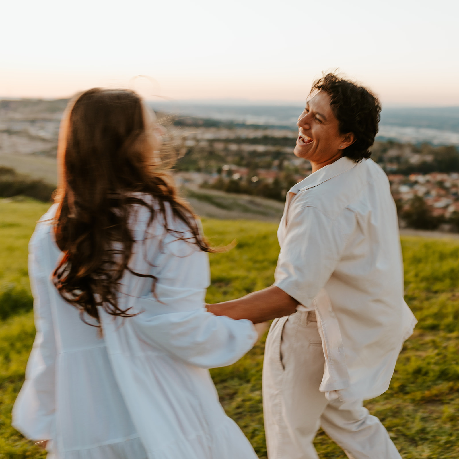 A couple in linen clothes laughs together in the California hills.