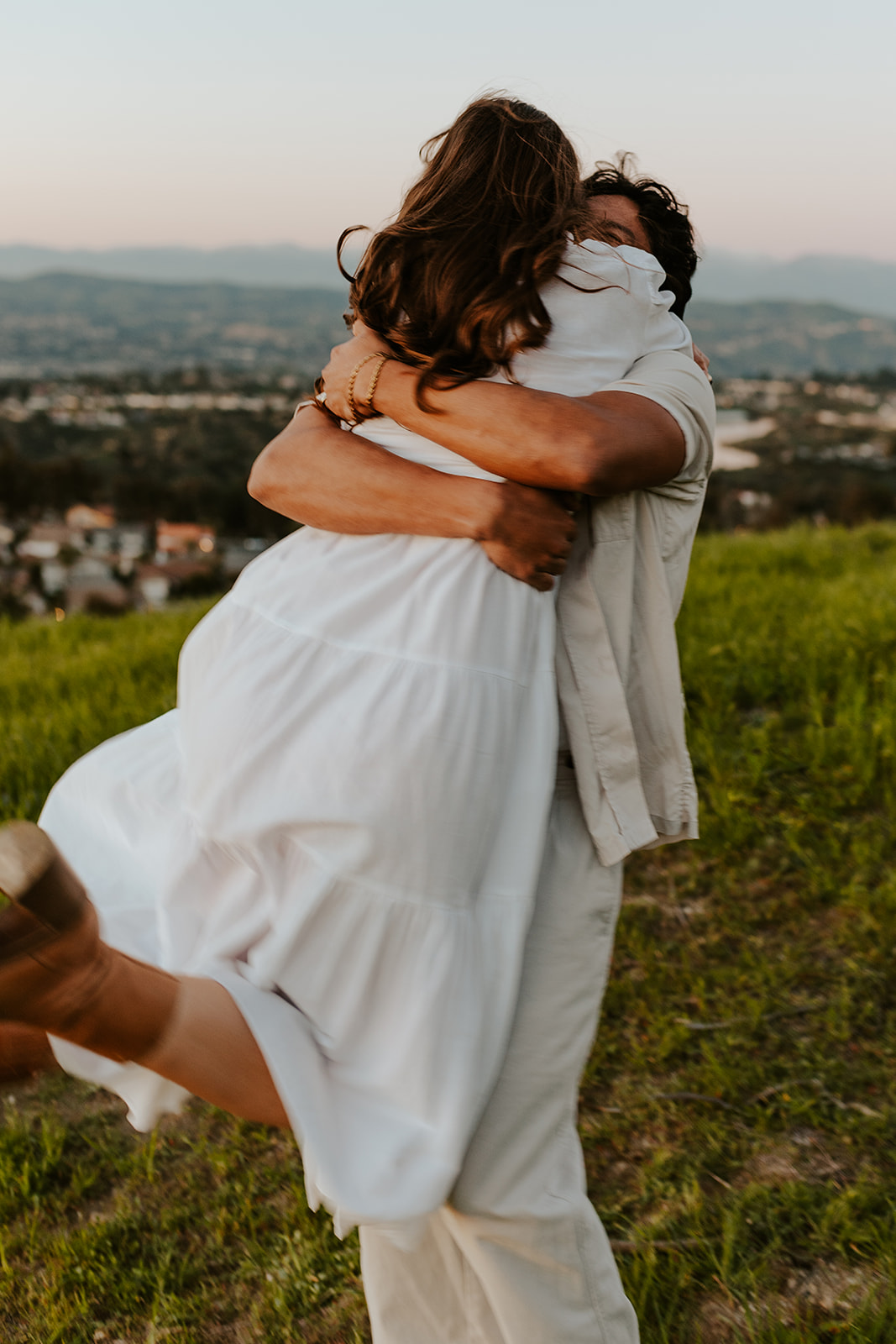 A couple in linen clothes embraces at sunset in the California hills.