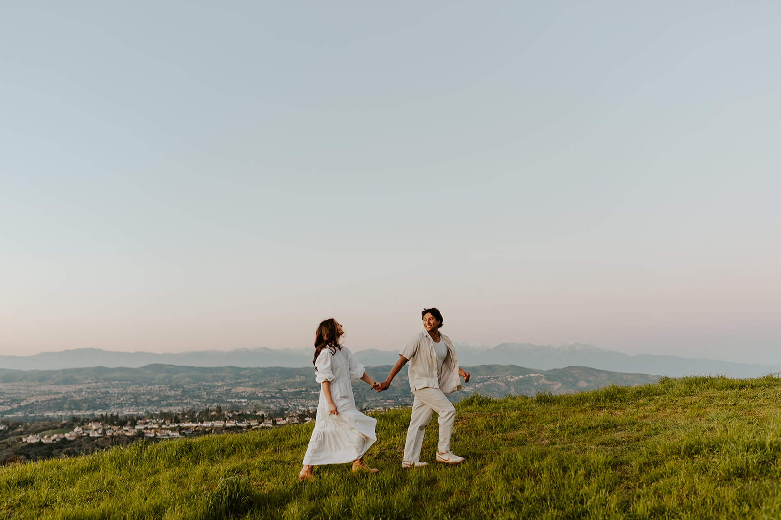 A couple in linen clothes walks at sunset in the California hills.