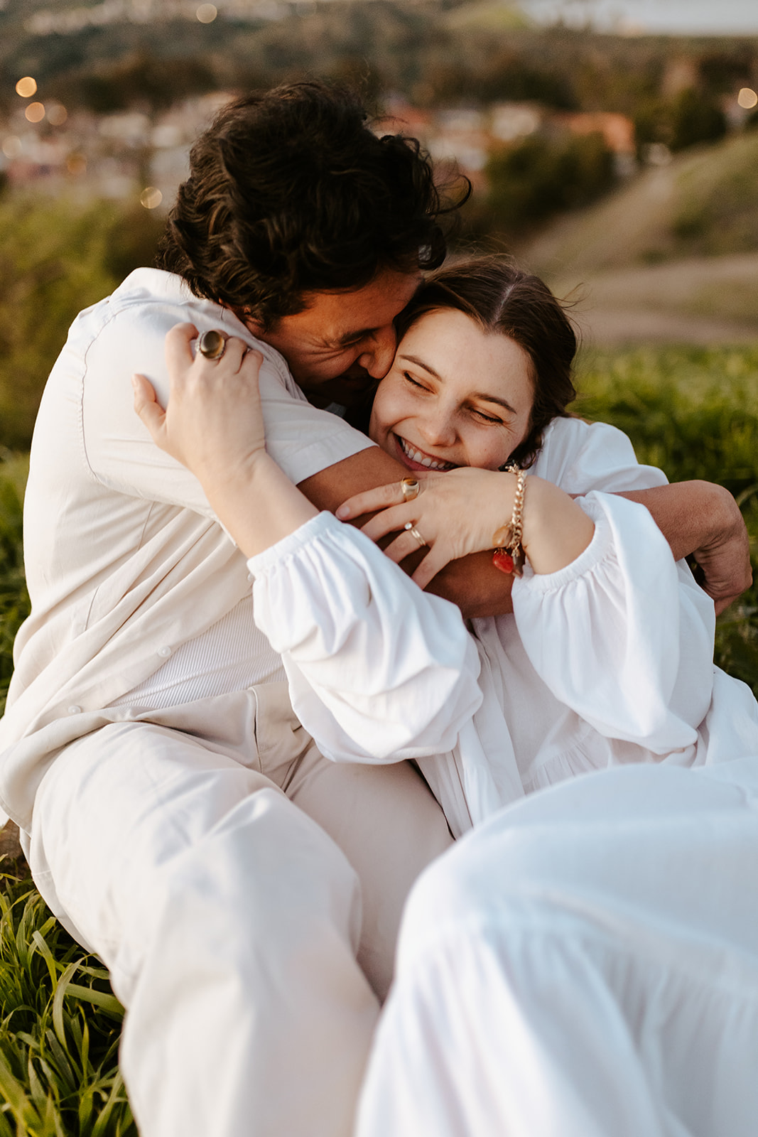 A couple in linen clothes snuggles at sunset in the California hills.