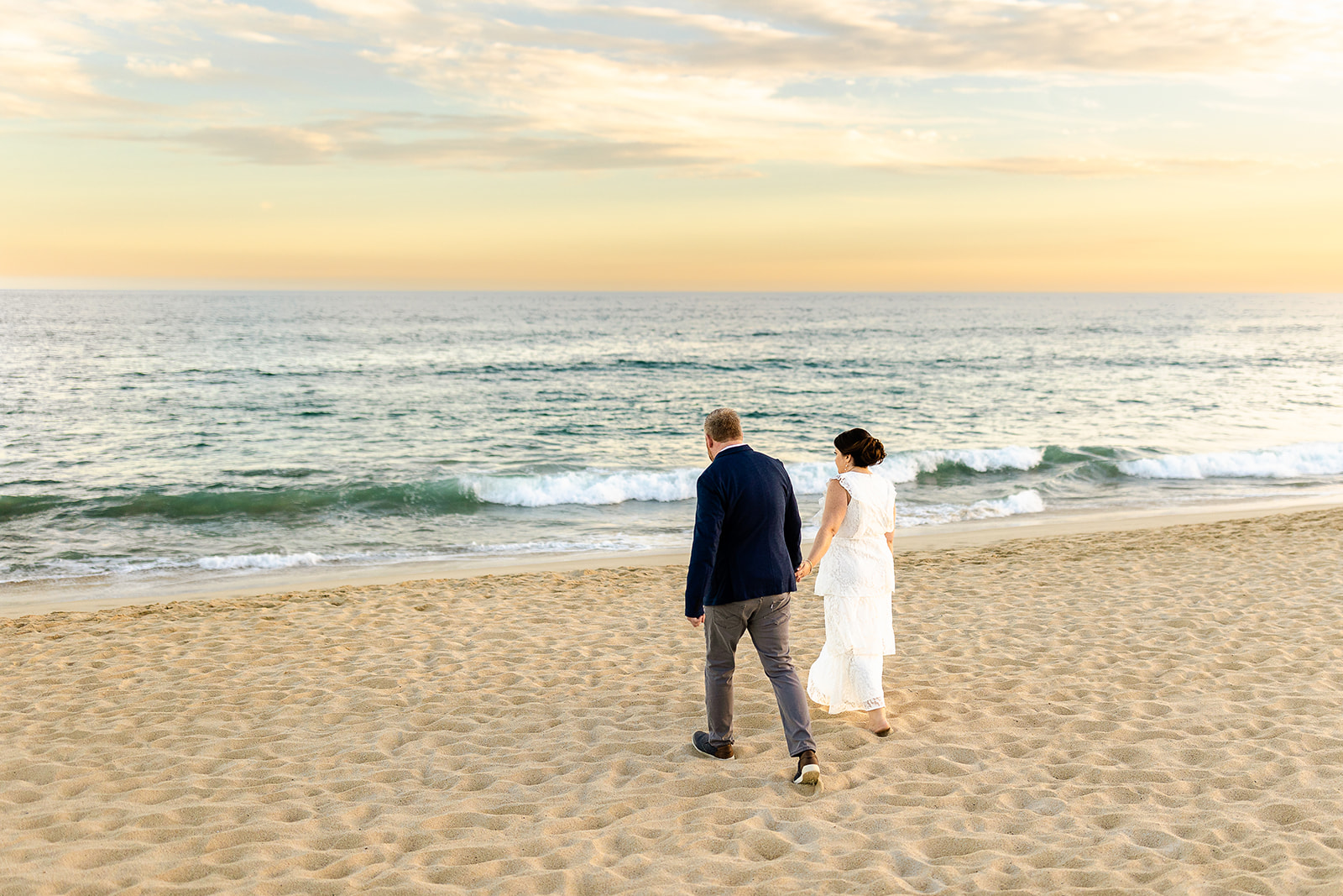 Couple holding hand and walking on the beach toward the ocean