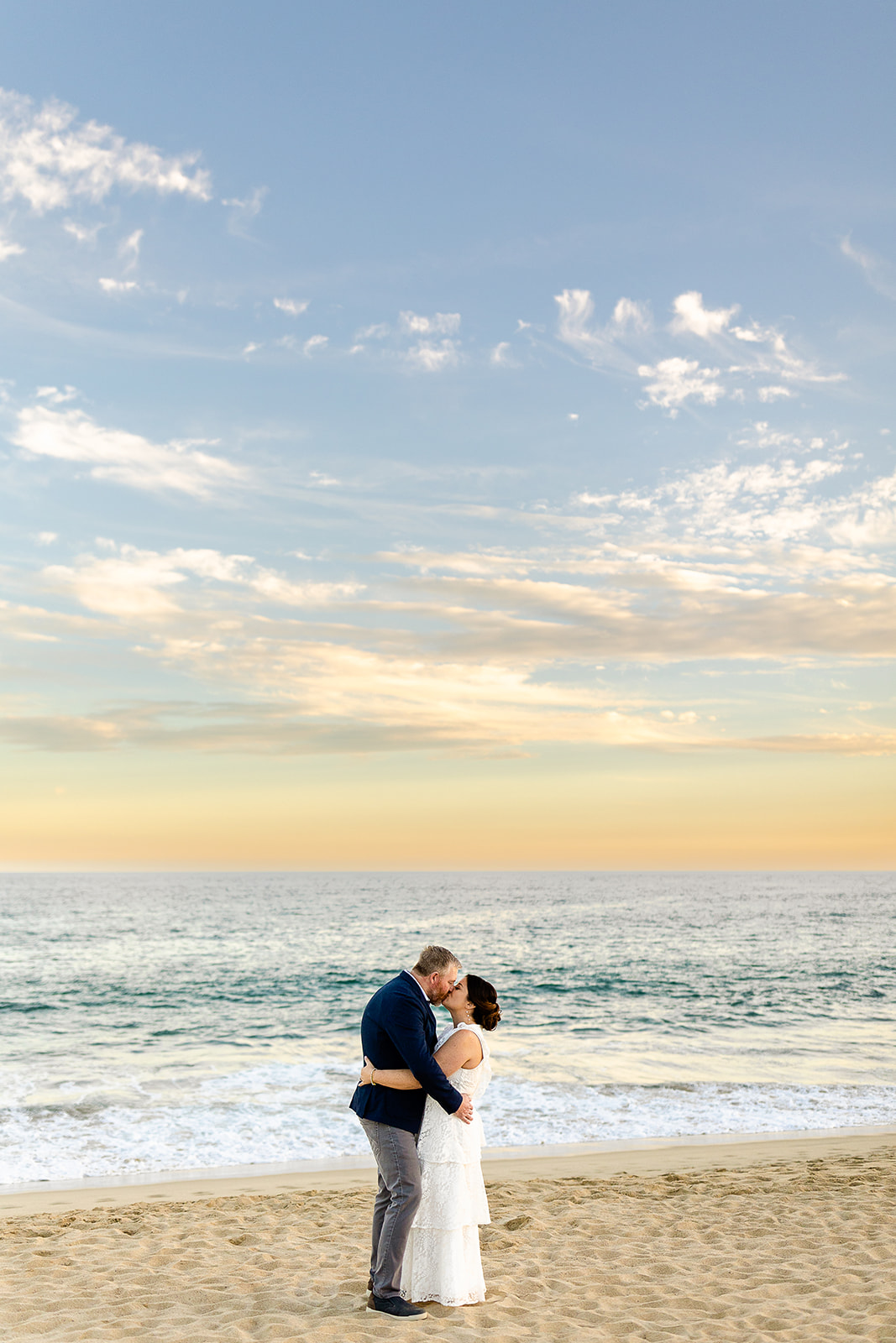 Couple hugging and kissing on the beach with the ocean behind them