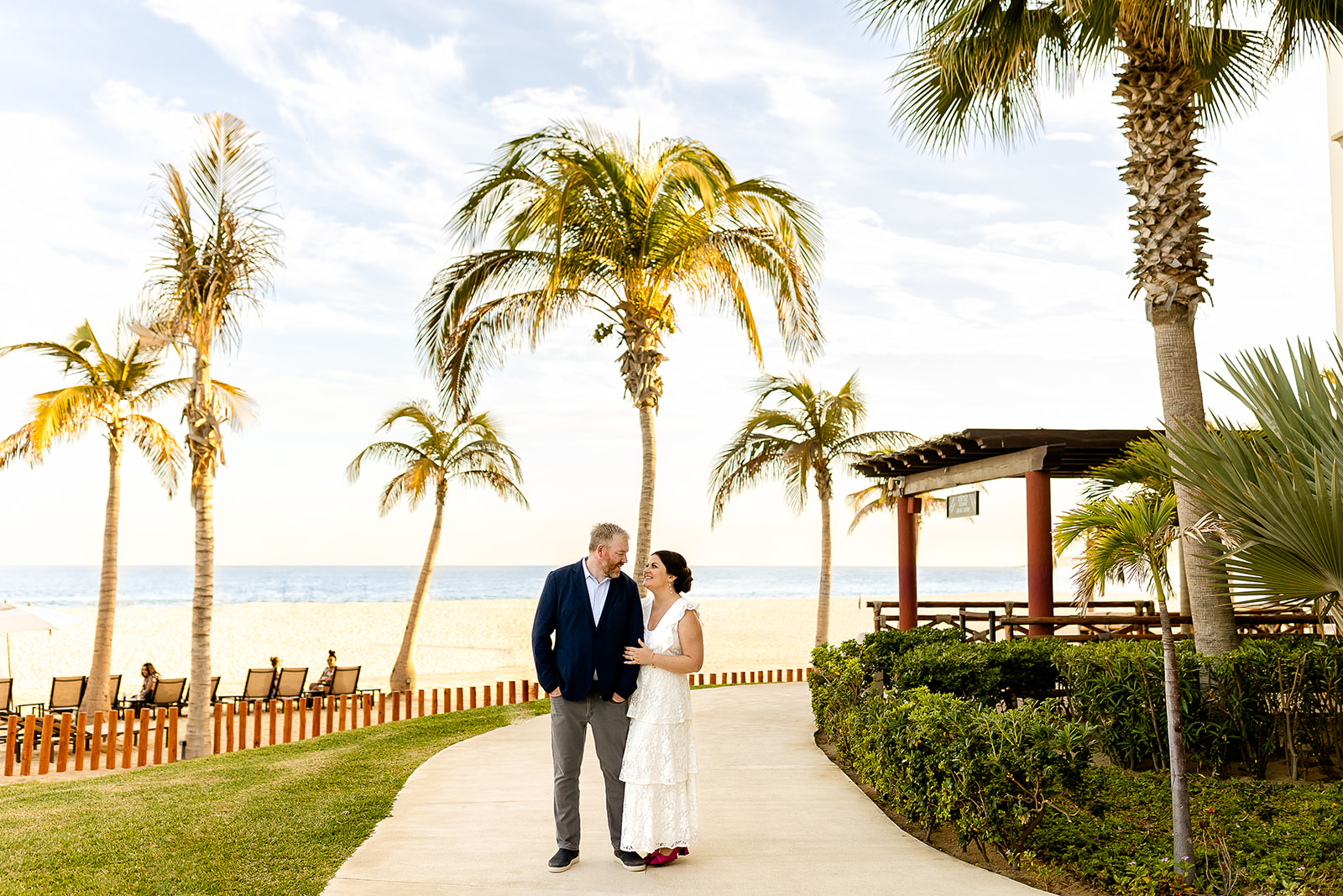 Couple standing holding hands and smiling with palm trees behind them