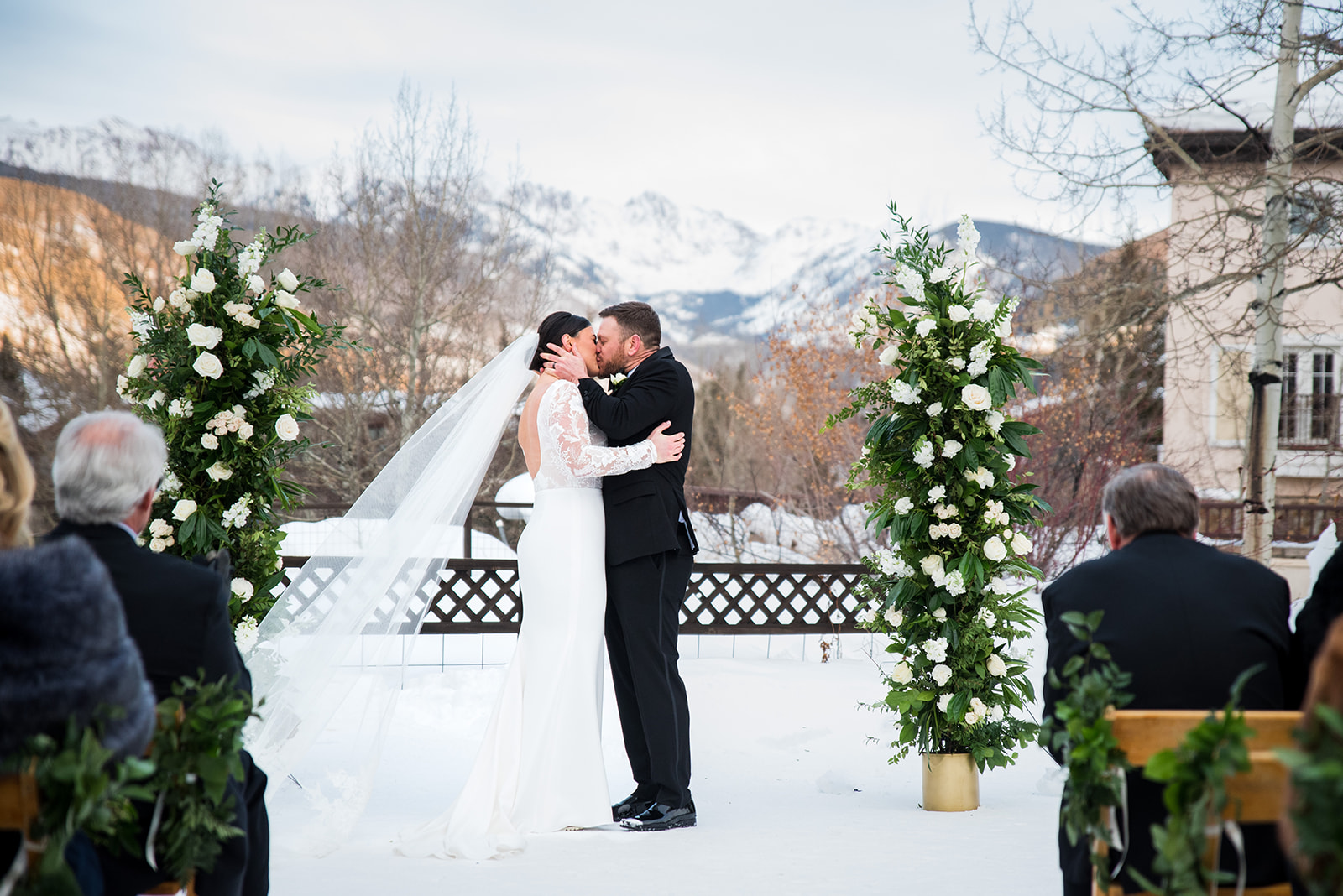 Bride and groom share first kiss at outdoor wedding ceremony in snowy Vail, Colorado.