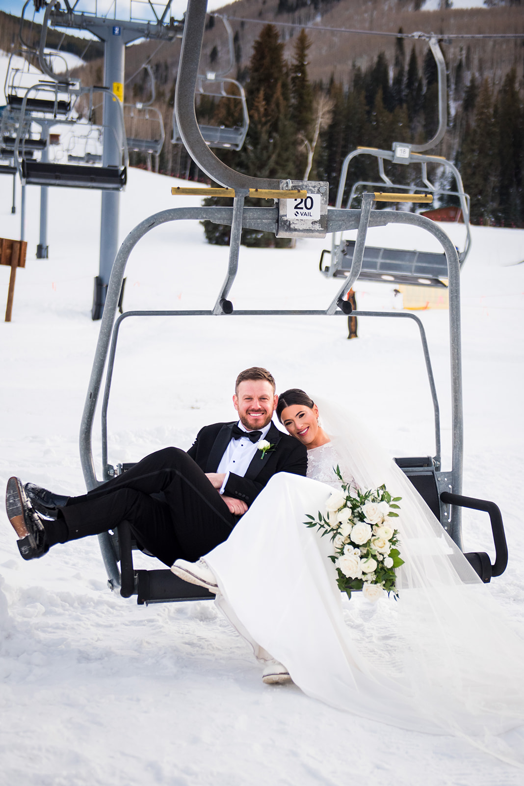 Bride and groom sit relaxed and smiling on a ski lift in Vail, Colorado.