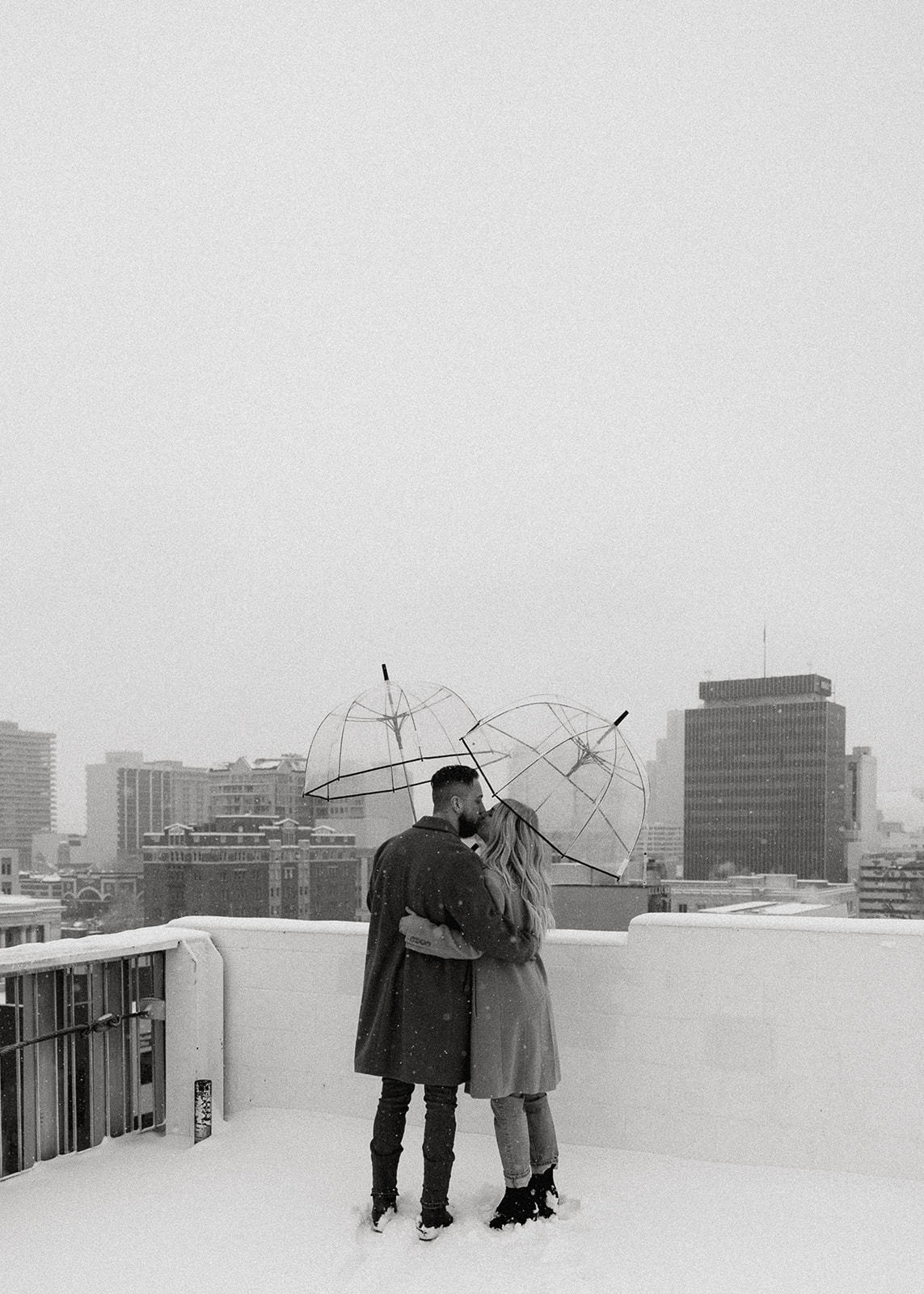 A couple snuggled up in the snow on the rooftop of a downtown reno parking garage. A black and white photographer. 