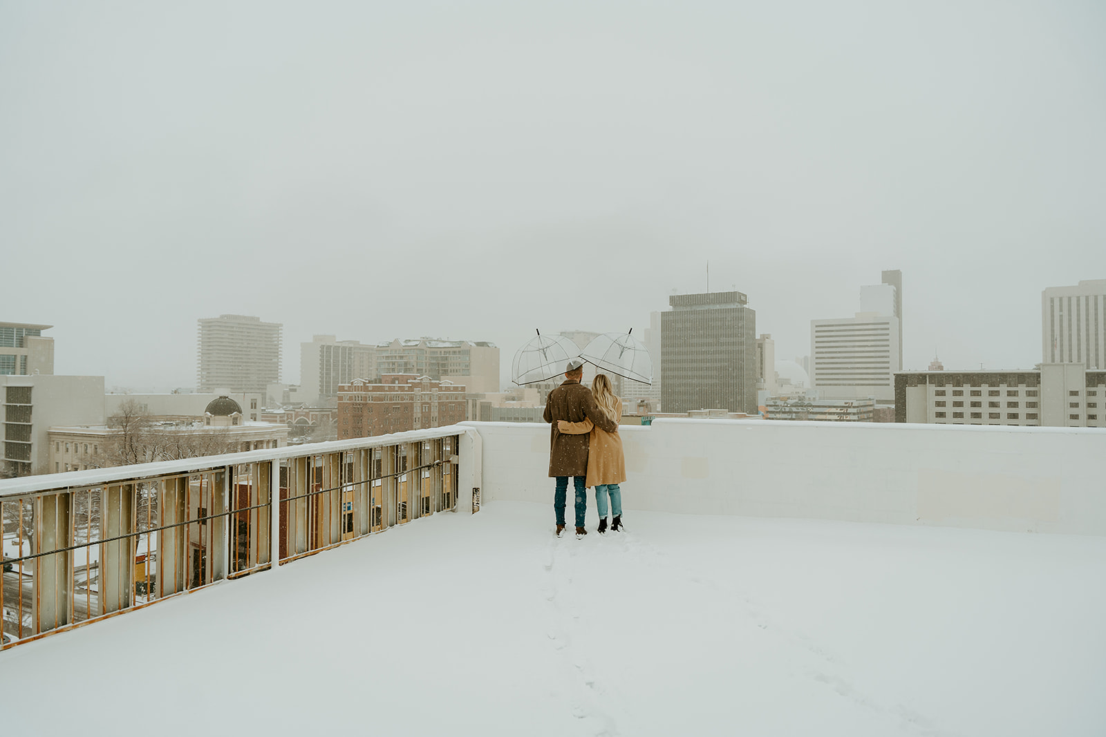 a wide angle shot photo of a dressed up couple snuggled up on a rooftop garage admiring the snow.