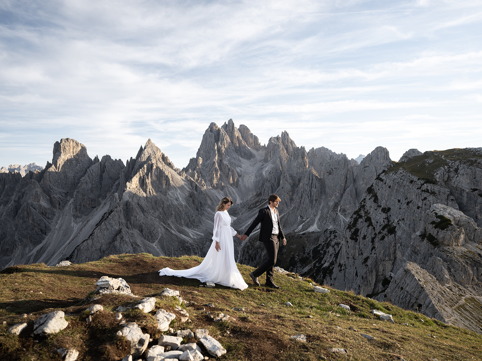couple walking in the dolomites in their wedding outfits on their wedding day 