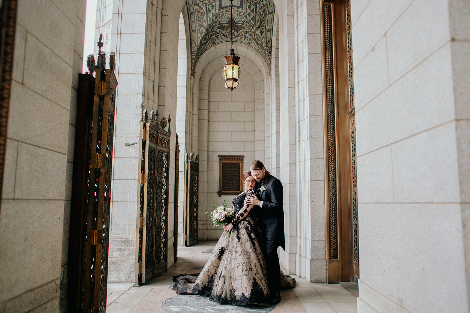 Elegant bride in black and lace gown with her husband, stand in front of the downtown St. Louis library