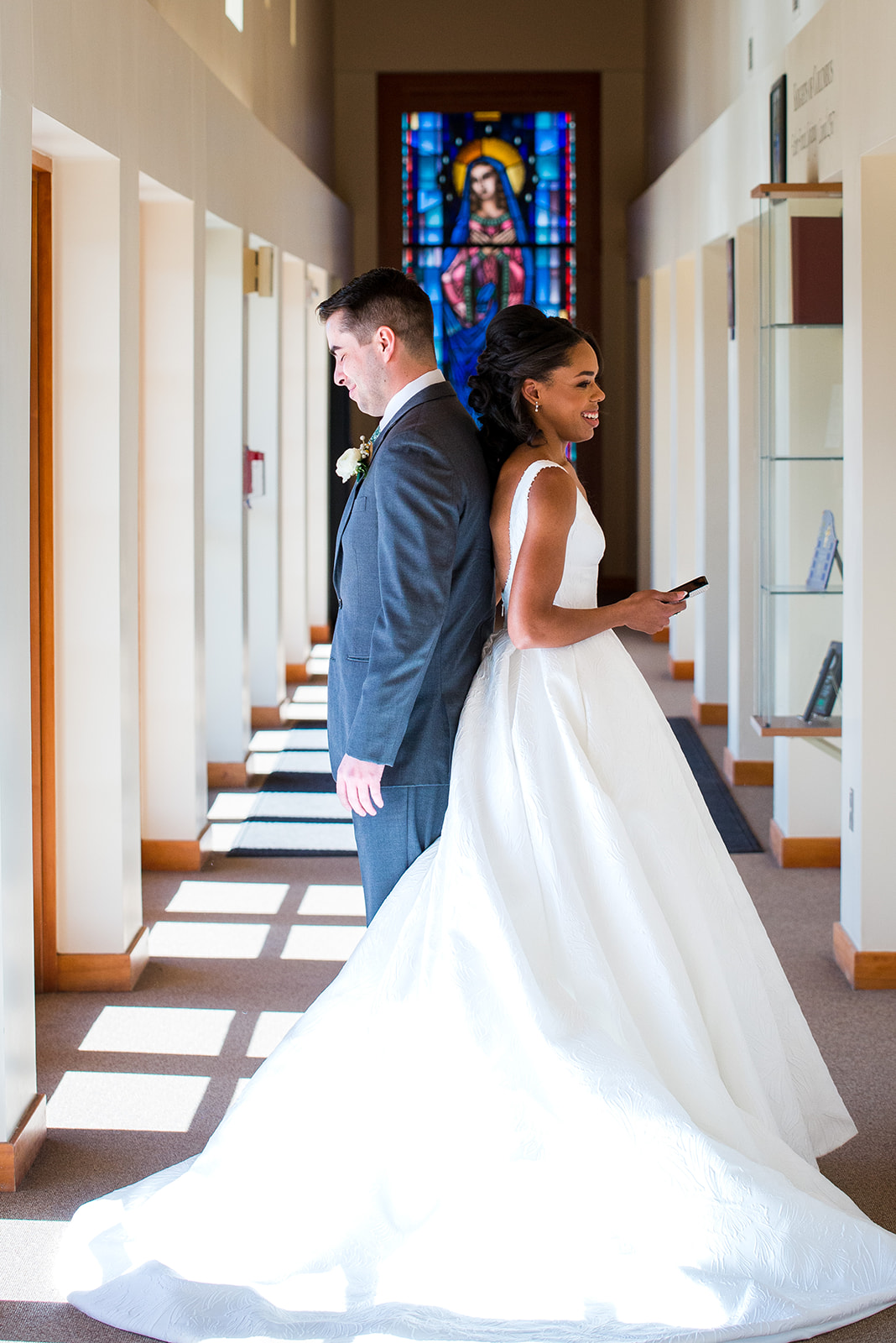 Bride and groom stand back to back in the hallway of the church, sharing a first touch and vows.