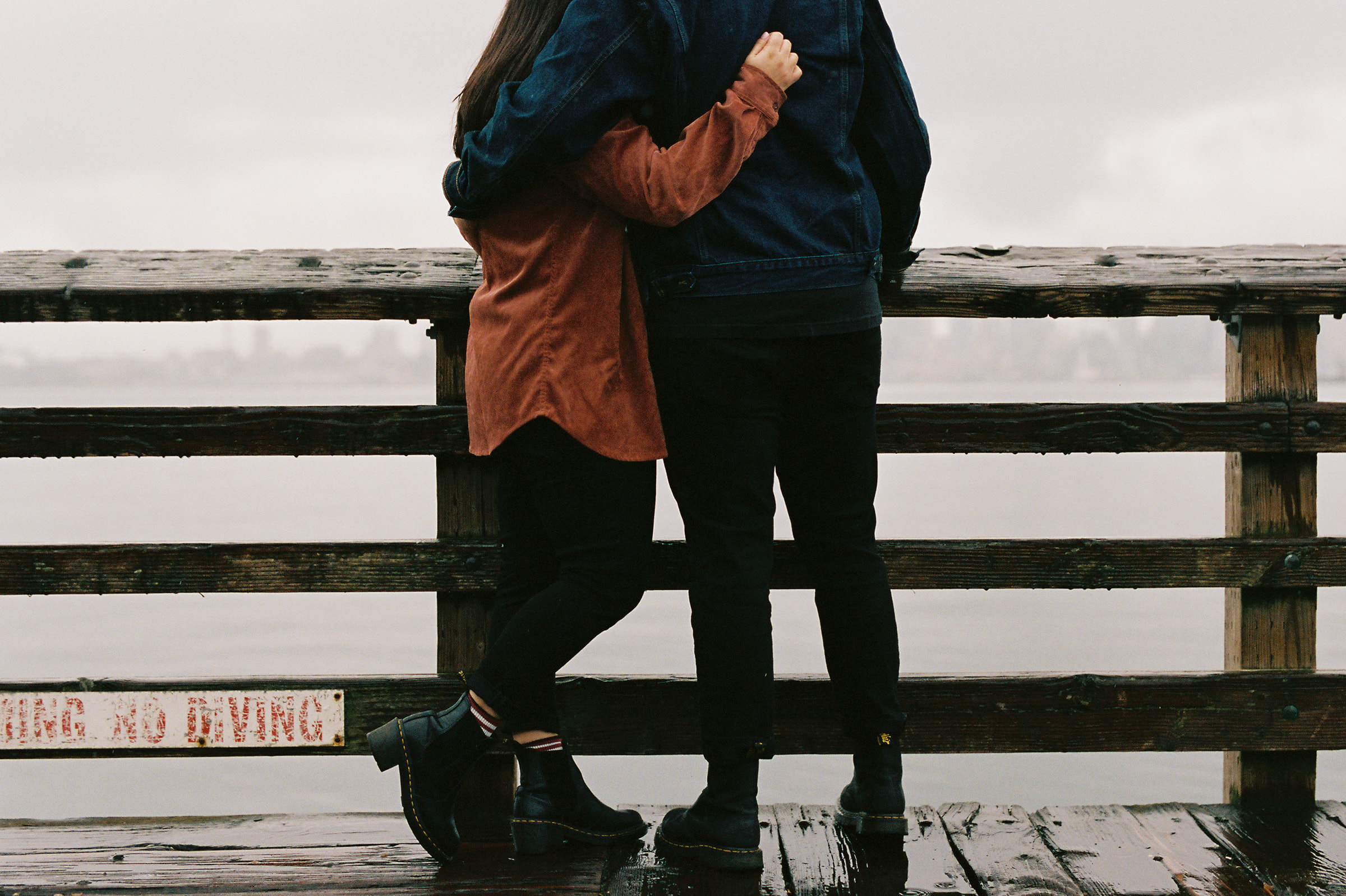 a couple cuddling on the pier while it's raining in an engagement photo