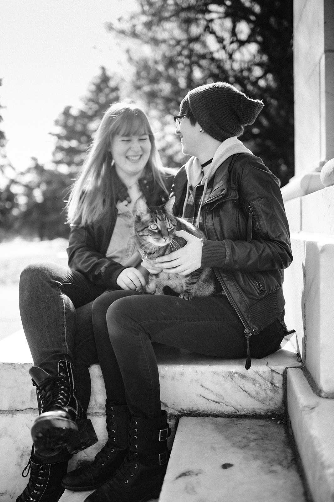 black and white photo of two women sitting on a step at a park holding their cat