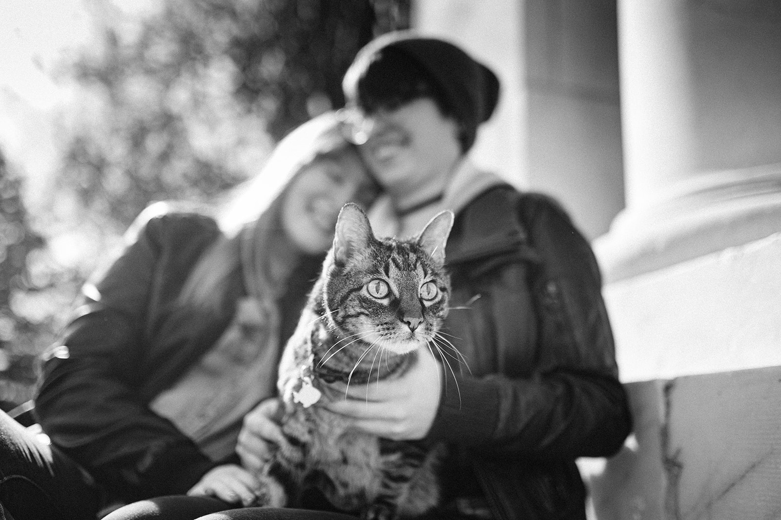 black and white photo of two women leaning on each other while holding their cat 